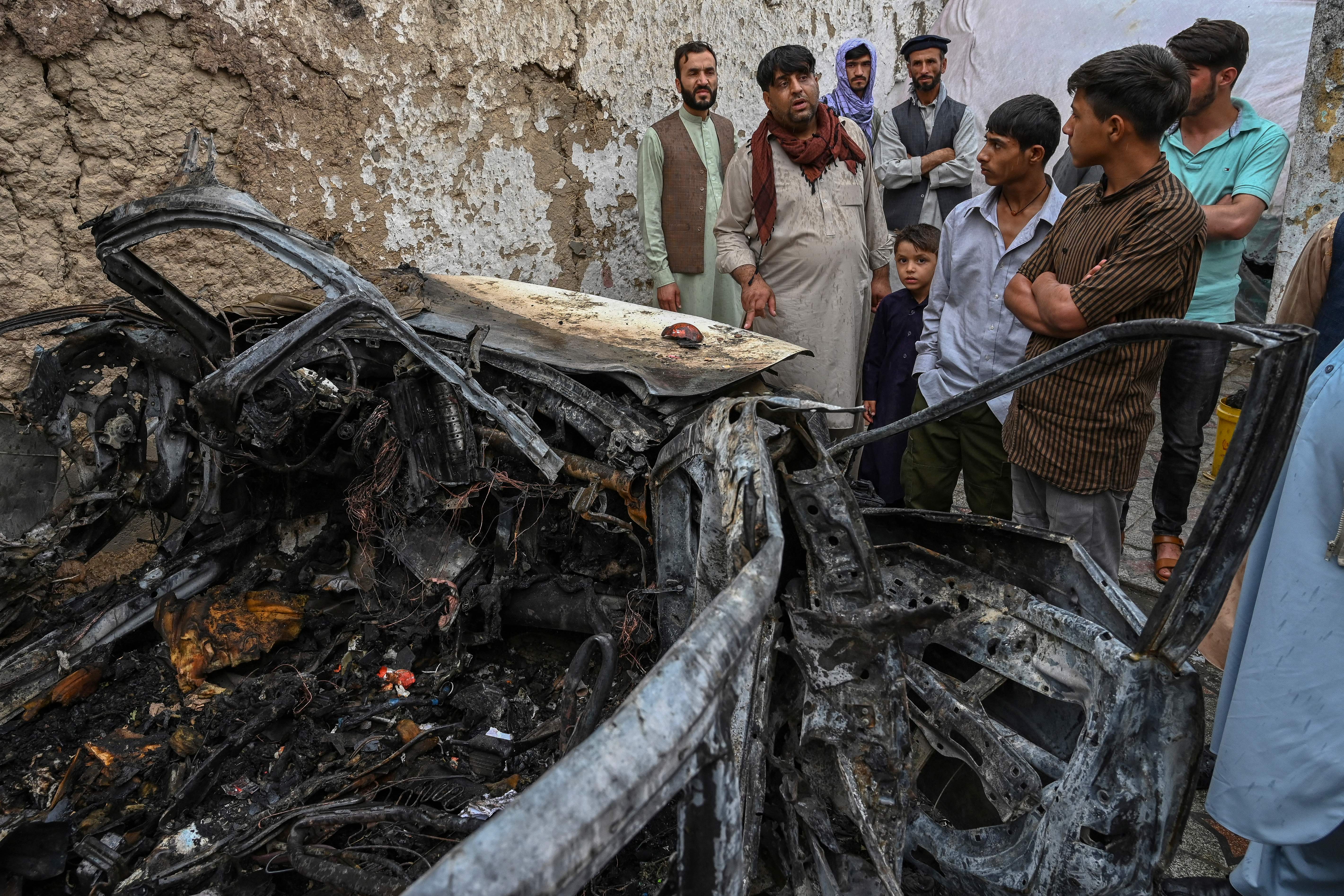Afghan residents and family members of the victims gather next to a damaged vehicle inside a house, day after a US drone airstrike in Kabul on 30 August, 2021.