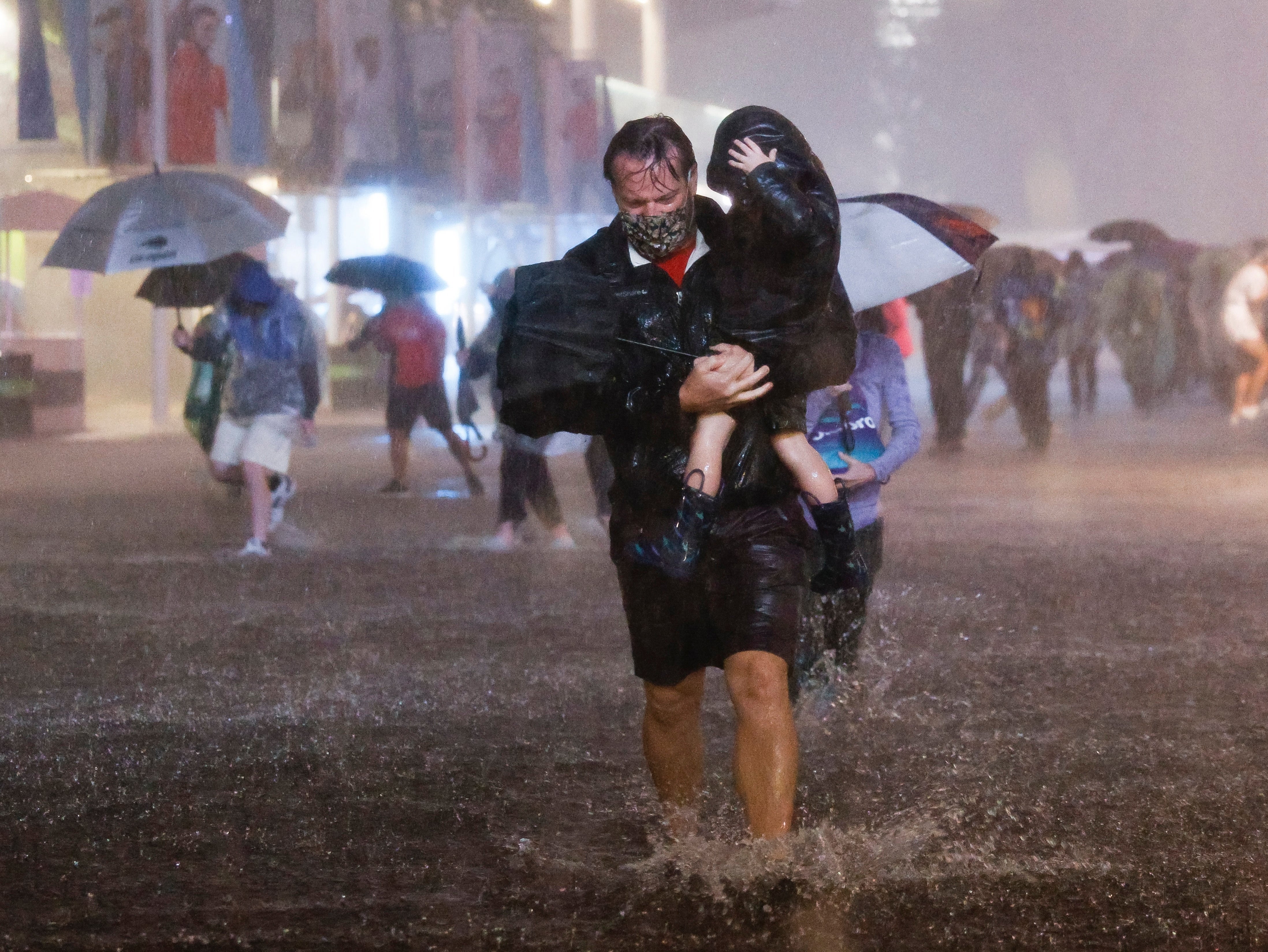 A father navigates heavy rains and flooded walkways at the Billie Jean King National Tennis Centre, in New York, while carrying his child