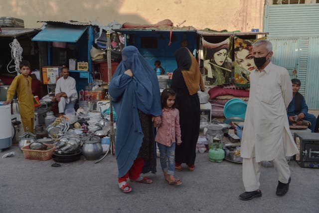 <p>A burqa clad Afghan woman looks for items to buy at a shop displaying used household items for sale at a market area in Kabul on 25 August 2021 </p>