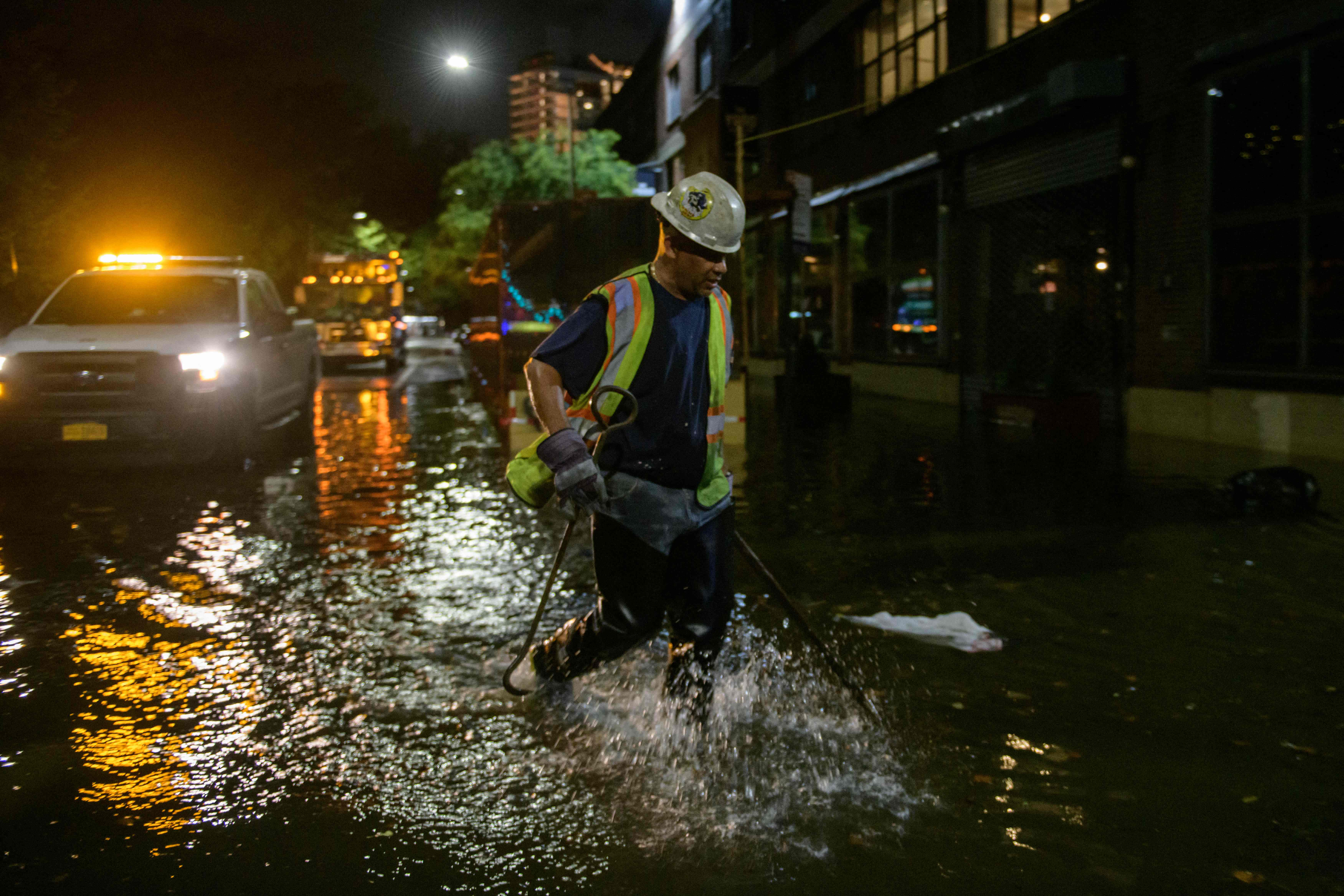 A worker unblocks drains on a street affected by floodwater in Brooklyn, New York early on September 2, 2021, as flash flooding and record-breaking rainfall brought by the remnants of Storm Ida swept through the area