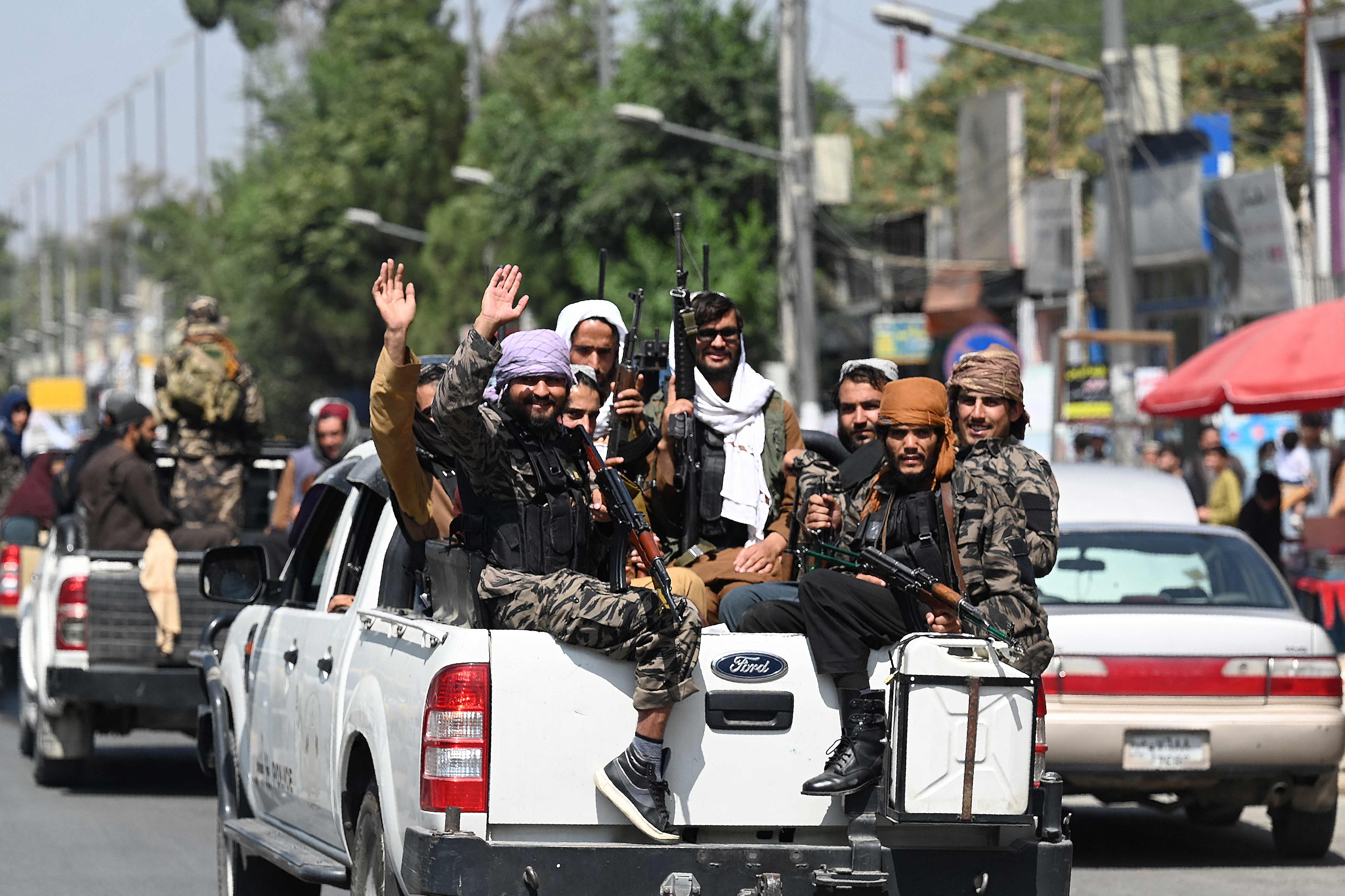 Taliban fighters wave as they patrol in a convoy along a street in Kabul on Thursday