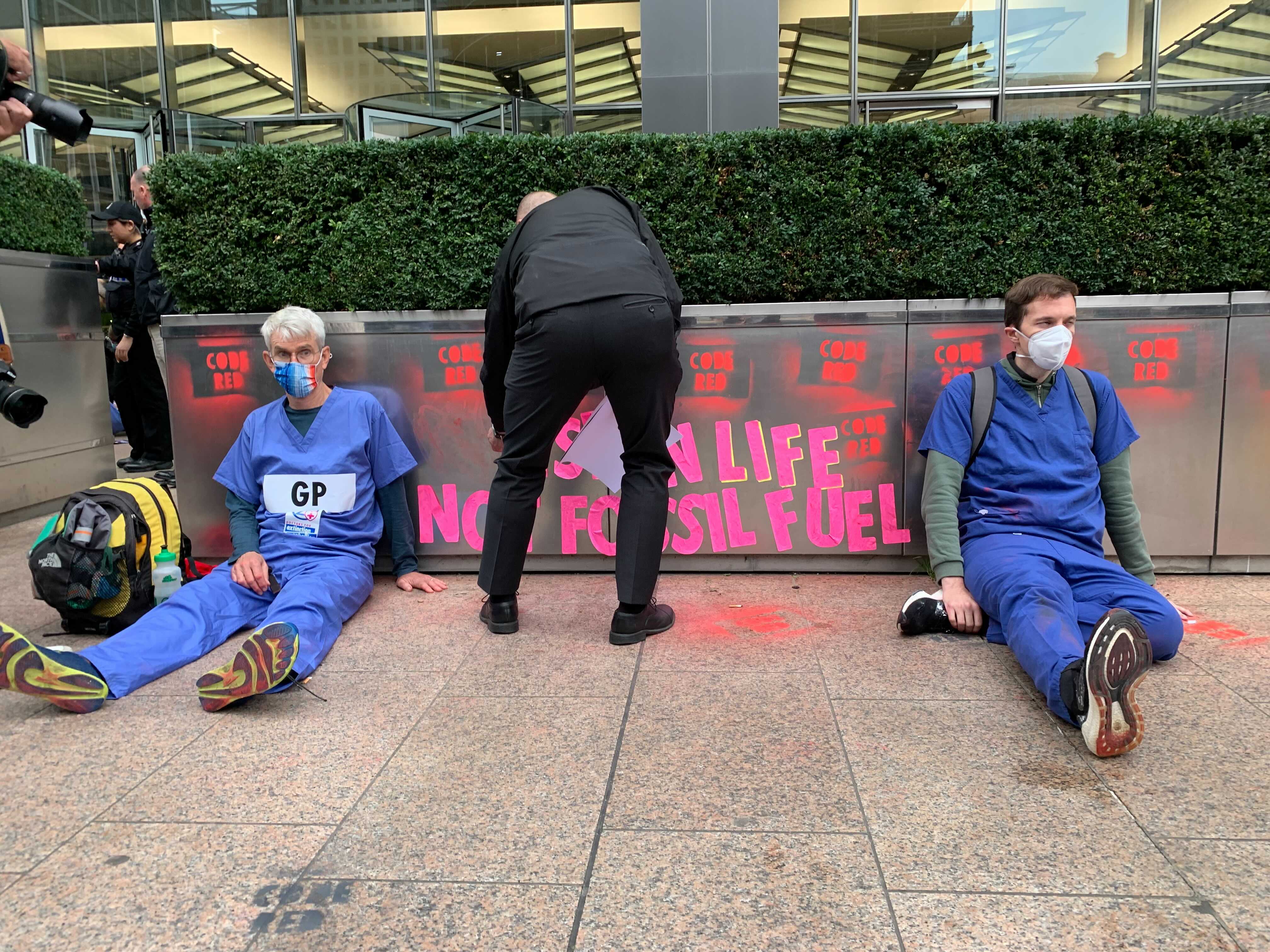 A police officer removes sticky notes put up by XR as two GPs sit glued to the ground outside JP Morgan’s building