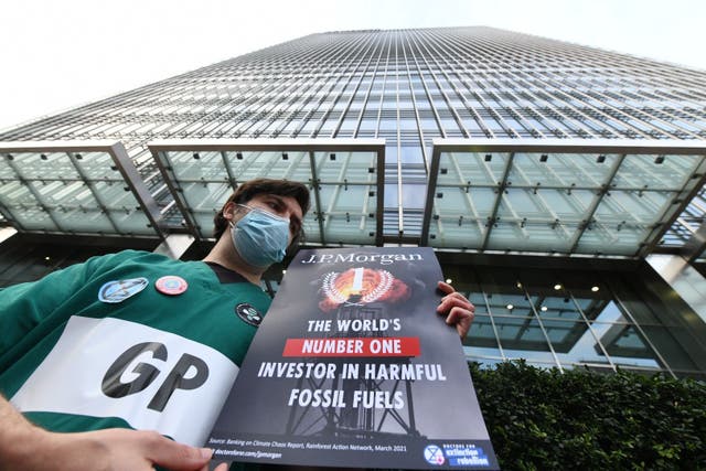 <p>A GP and member of Doctors for Extinction Rebellion holds up a sign outside JP Morgan Chase’s London HQ </p>