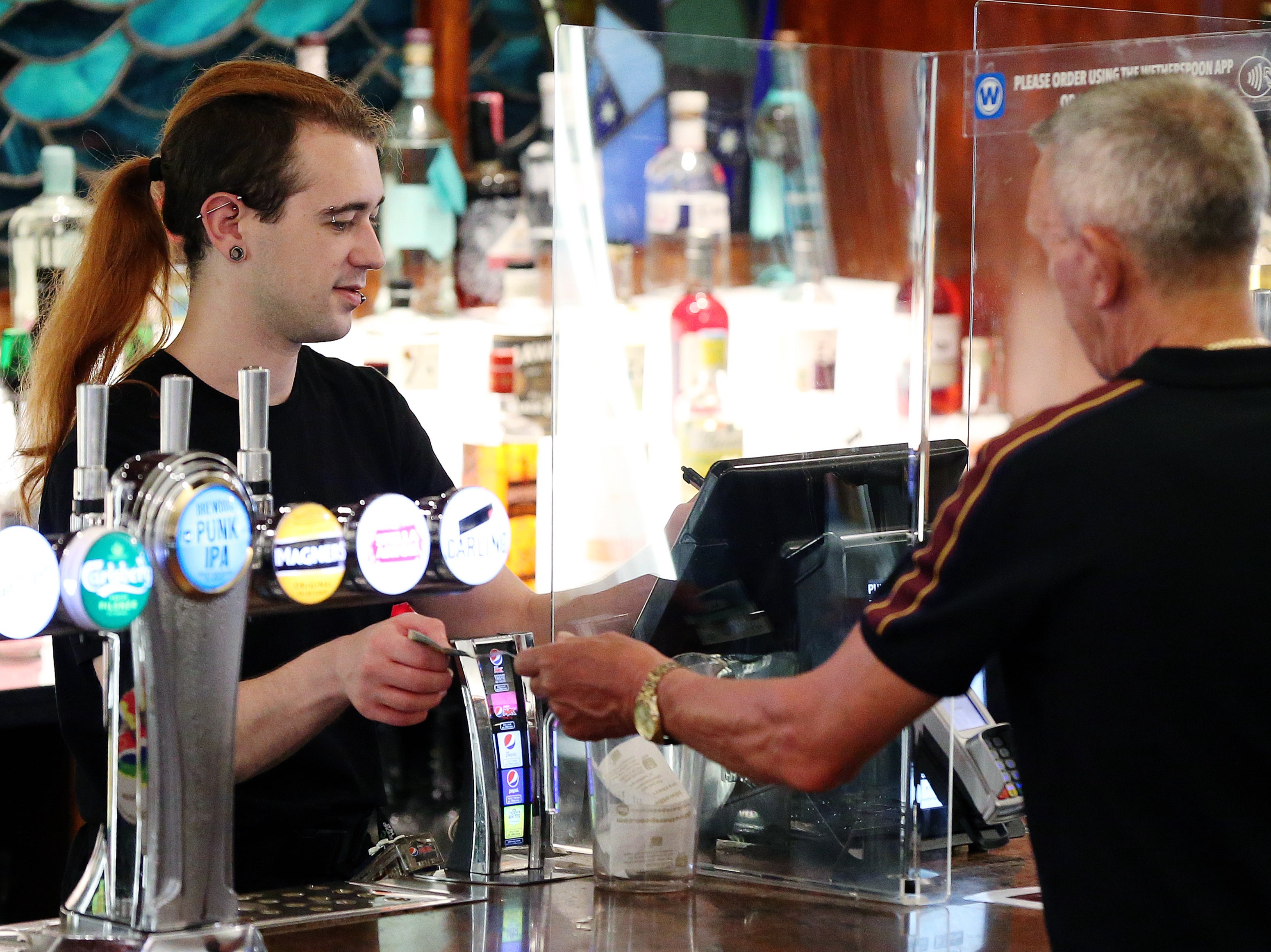 A customer hands a member of staff cash while paying for drink at a bar in Manchester, England