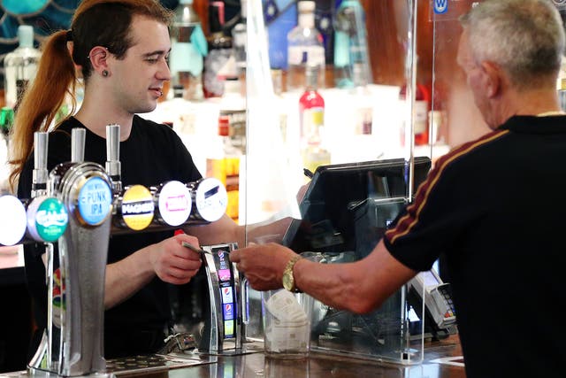 <p>A customer hands a member of staff cash while paying for drink at a bar in Manchester, England</p>