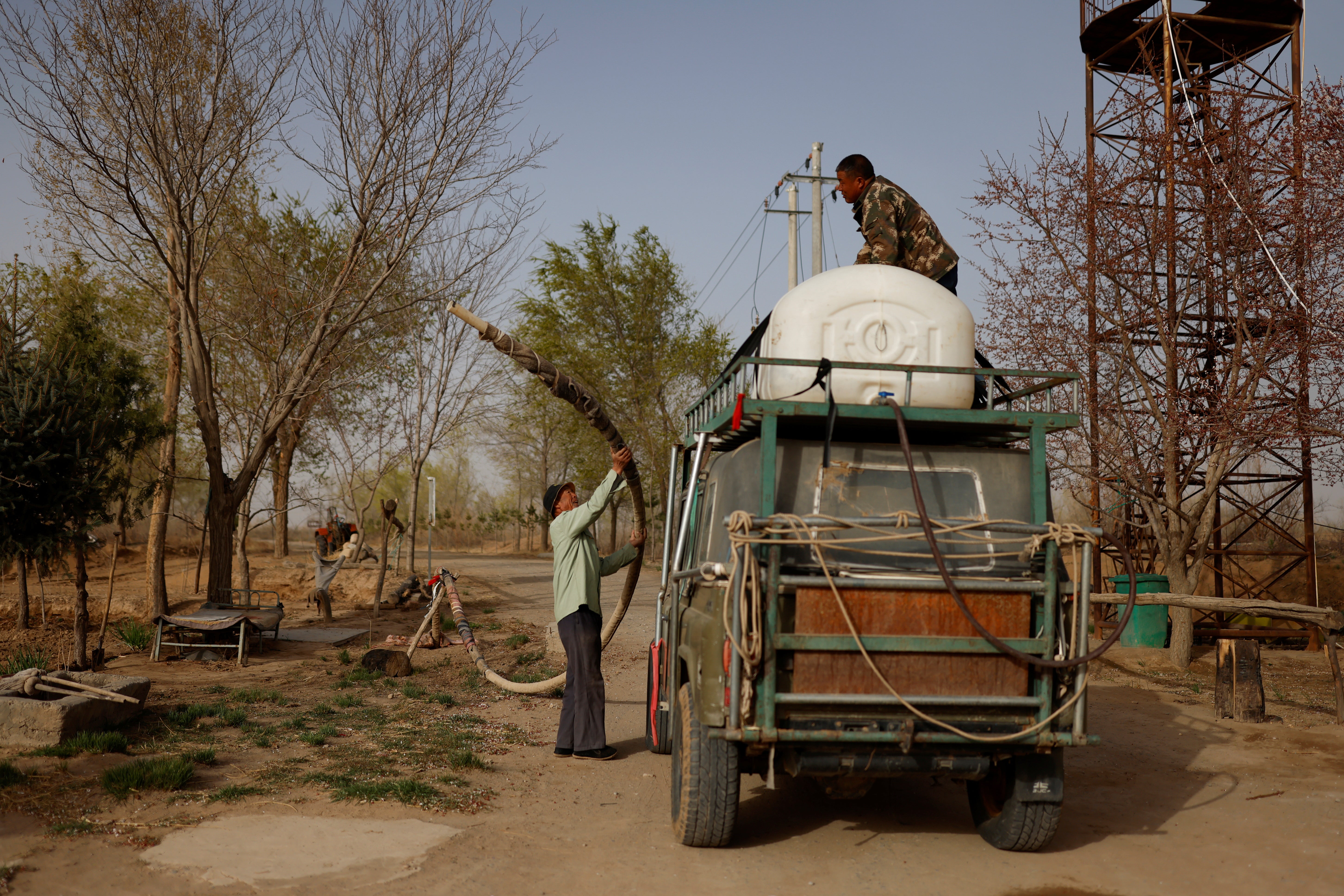 Wang Tianchang helps his son Wang Yinji fill a water tank on the roof of their truck before driving into the desert to plant trees