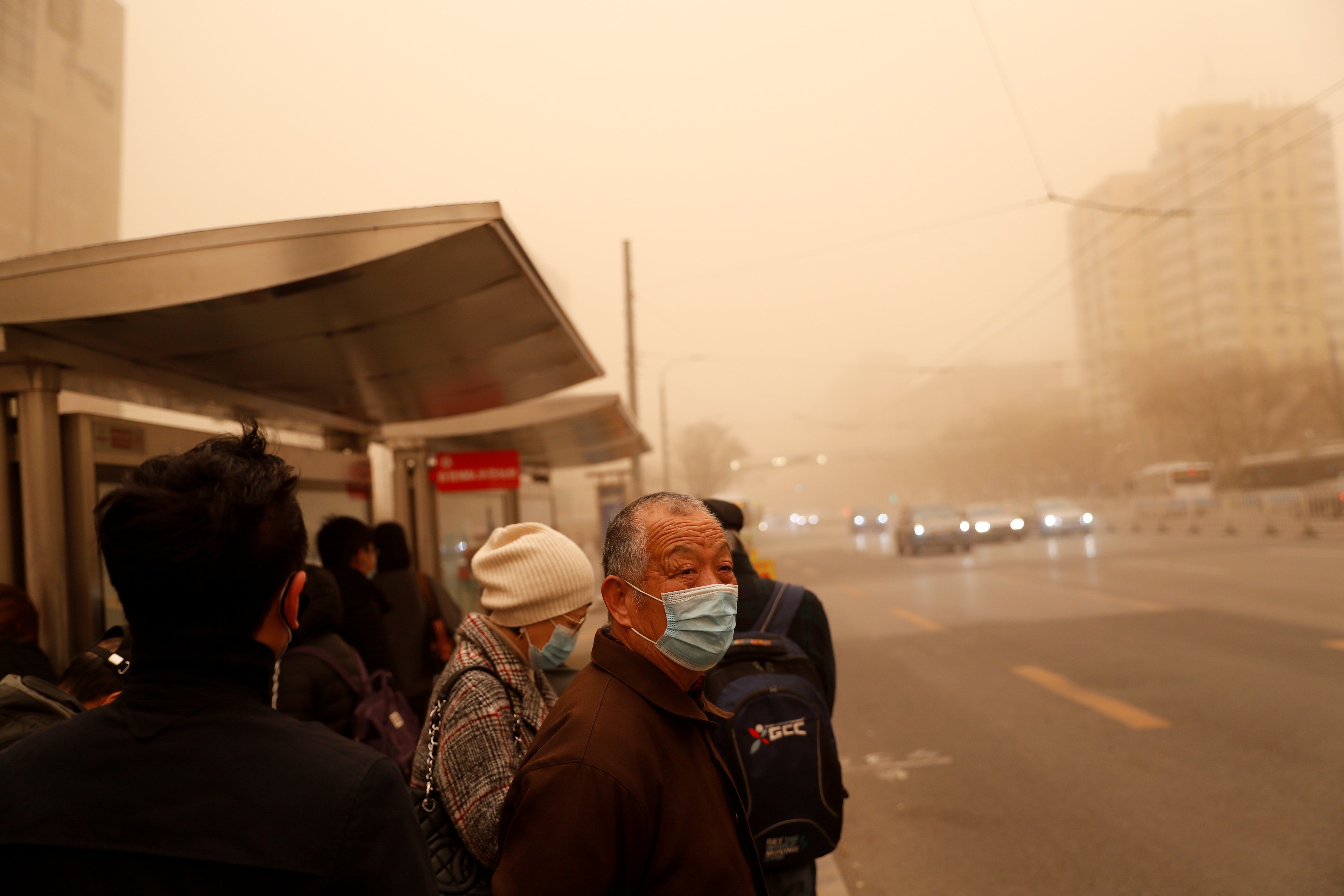 People wait for transportation at a Beijing bus stop as the city is hit by a sandstorm