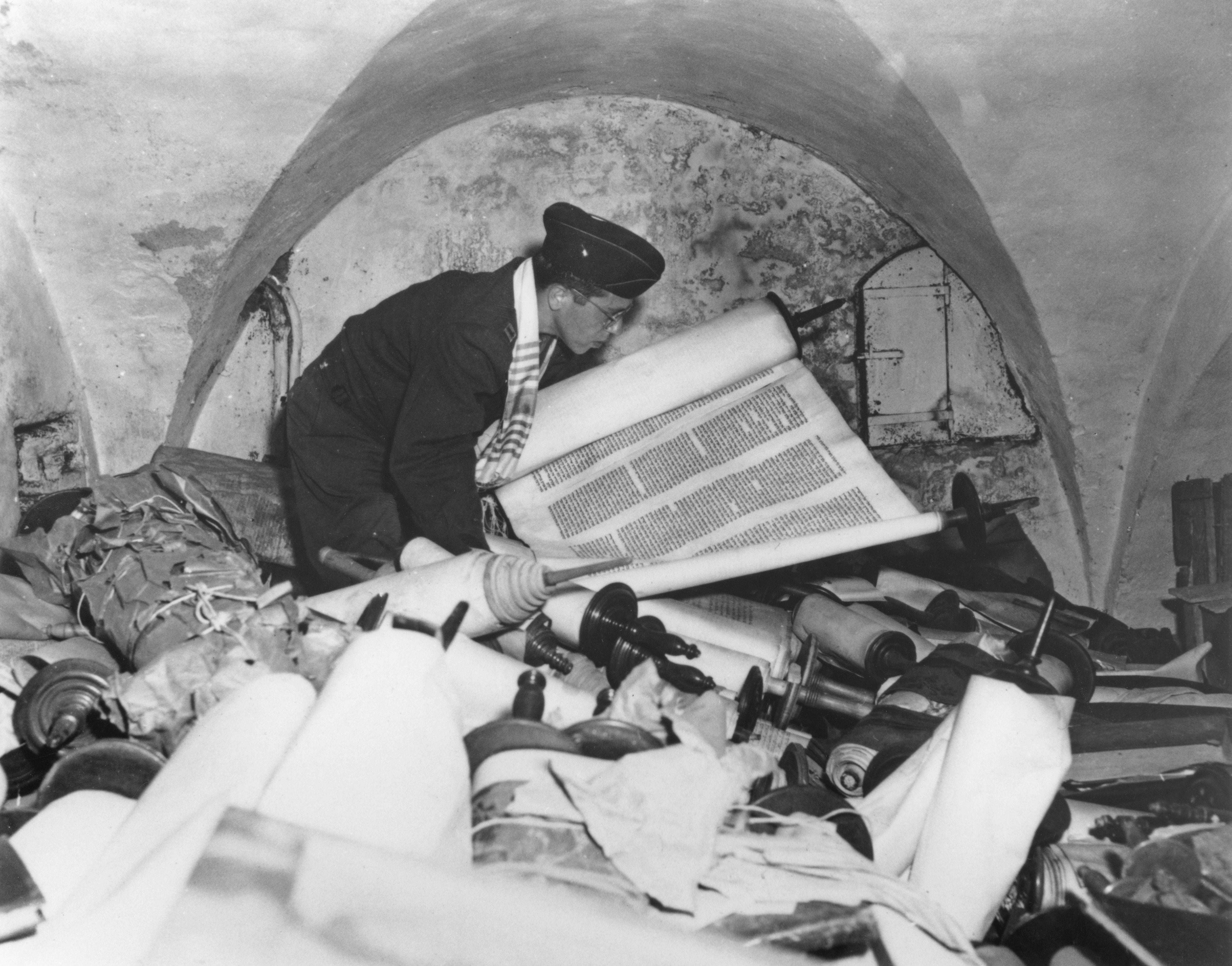 US Army chaplain Samuel Blinder examines one of hundreds of Jewish Sefer Torah scrolls, stolen from all over Europe by Nazi forces, and stored in the cellar of the Kaiser Wilhelm Institute of Anthropology, Human Heredity, and Eugenics (KWI-A) in Frankfurt, Germany, 6th July 1945