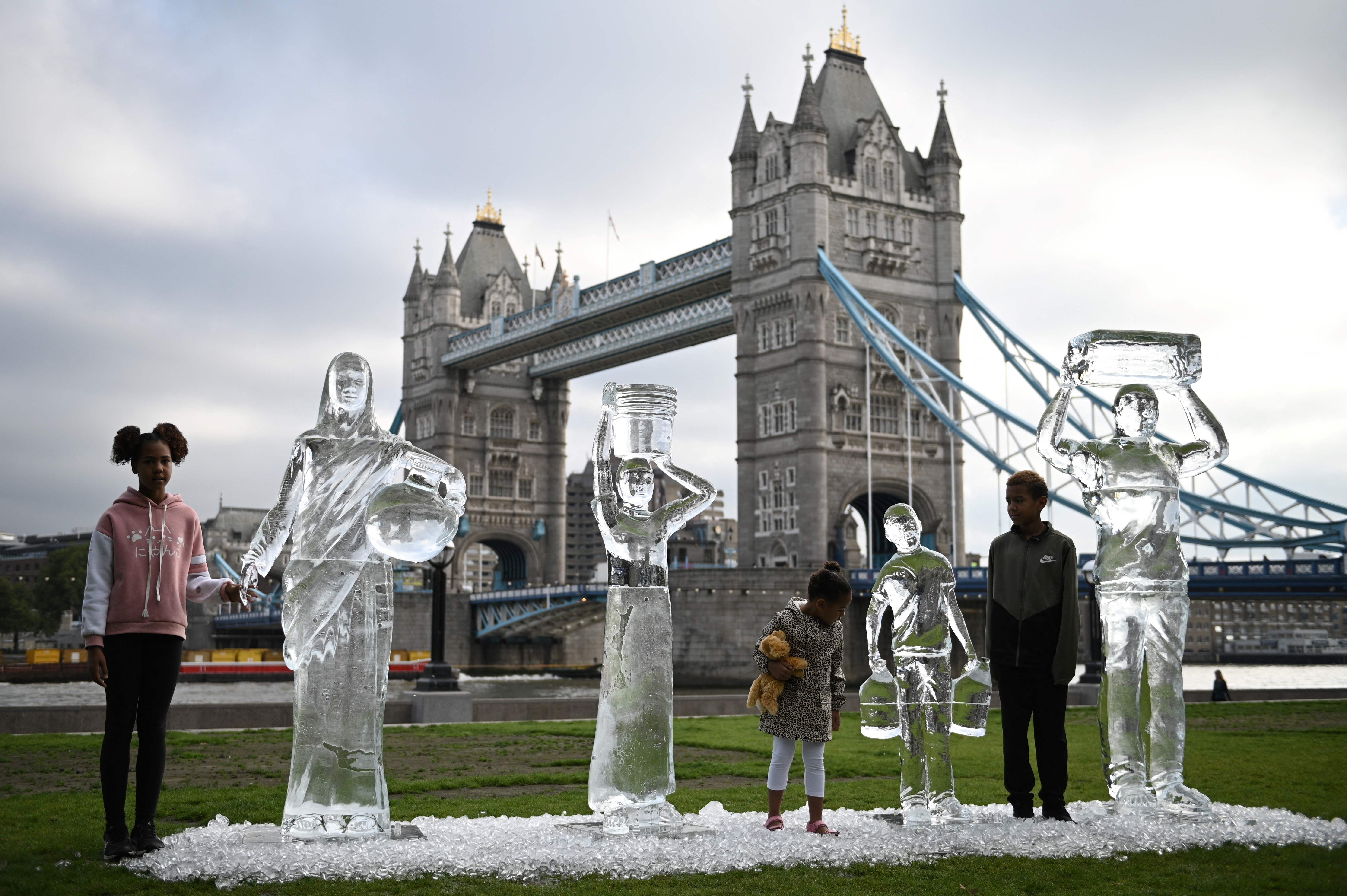 Children pose by ice sculptures depicting people collecting water by charity Water Aid to show the fragility of water and the threat posed by climate change in London