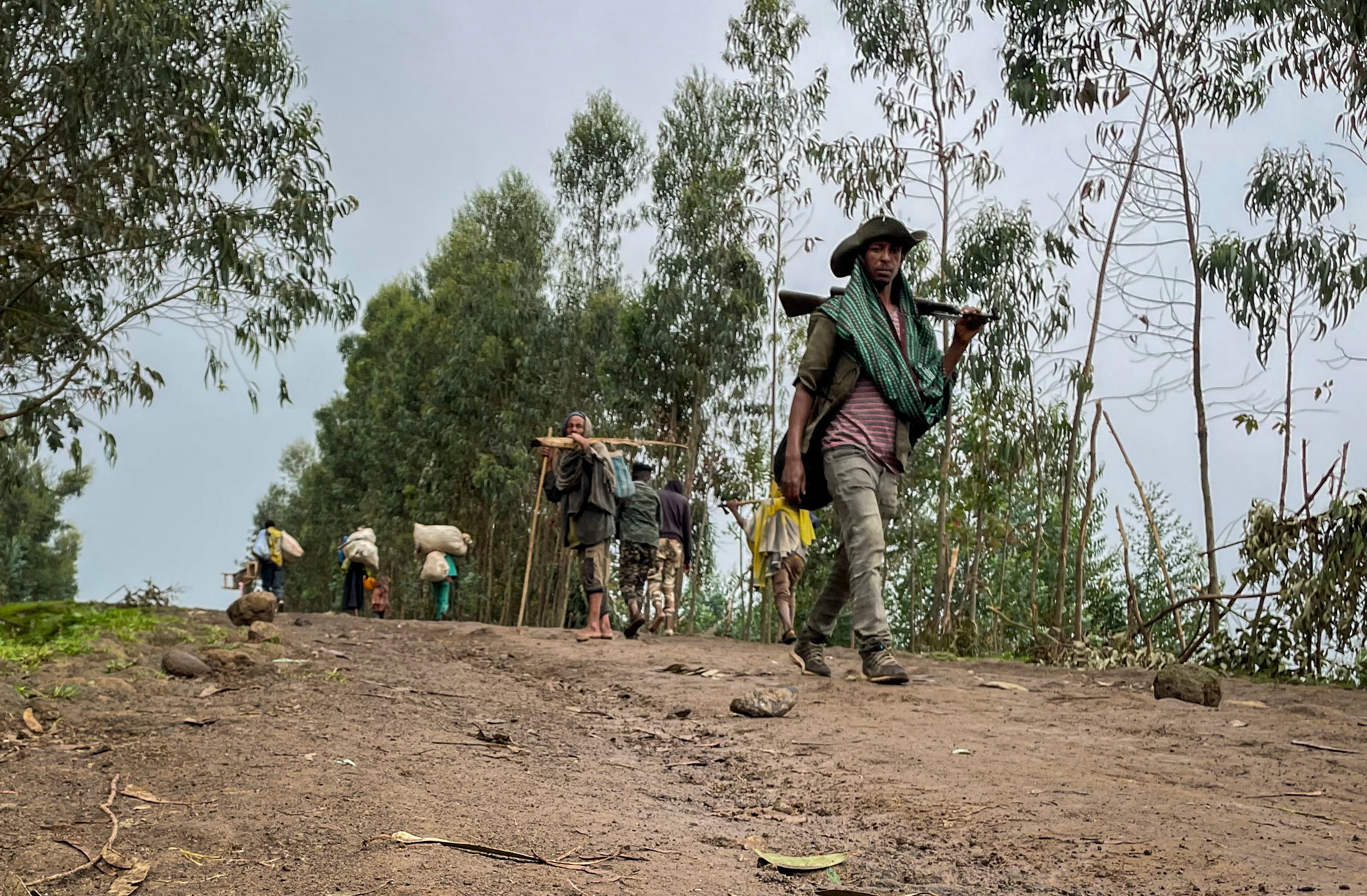 An unidentified armed militia fighter walks down a path as villagers flee with their belongings in the other direction, near the village of Chenna Teklehaymanot, in the Amhara region of northern Ethiopia