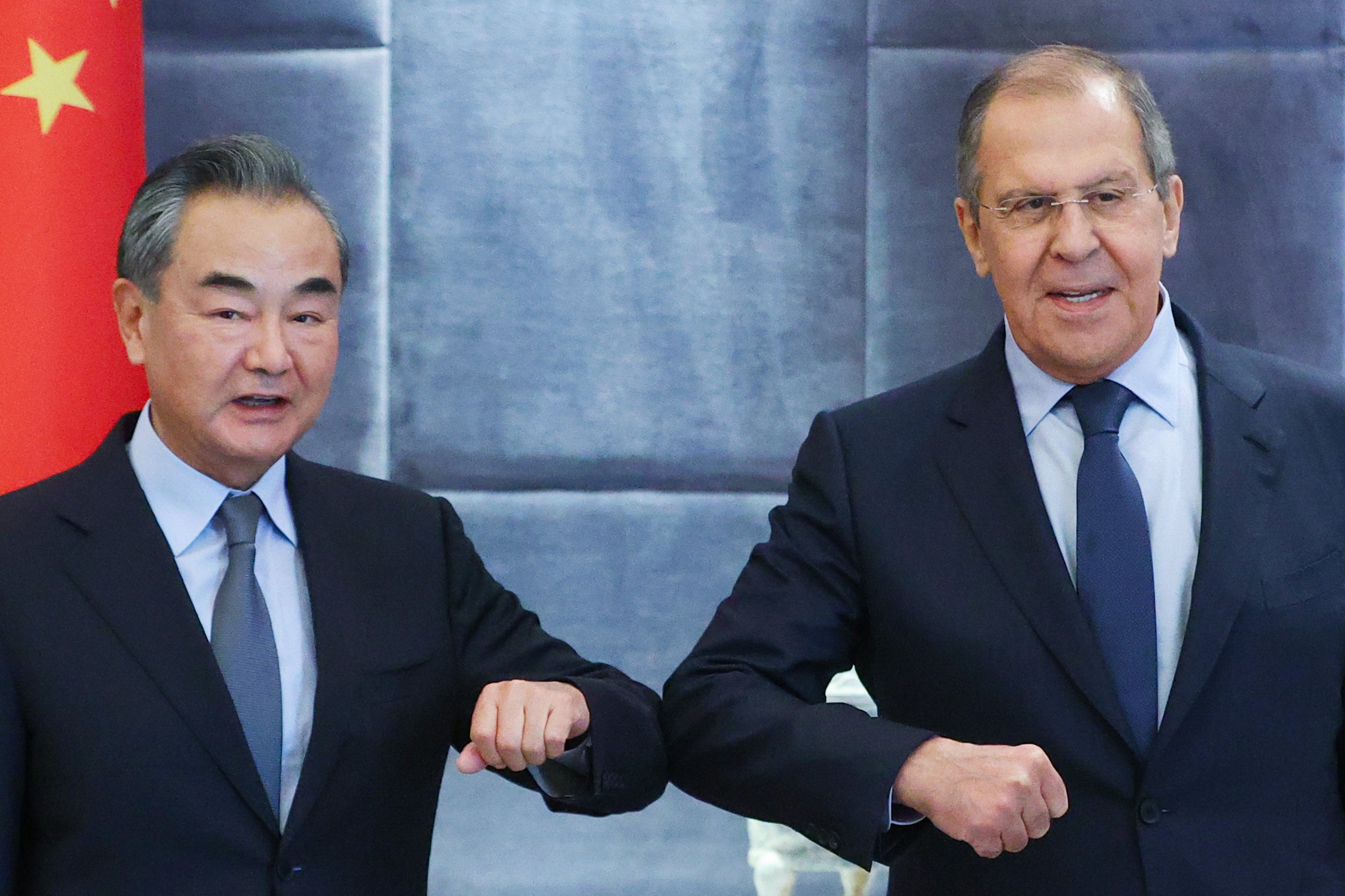China's Foreign Minister Wang Yi (L) and his Russian counterpart Sergei Lavrov bump elbows as they meet for talks