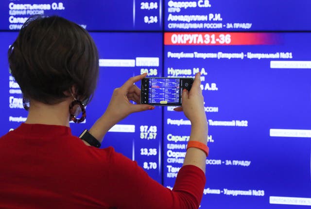 <p>A woman takes a picture of a screen displaying preliminary voting results</p>