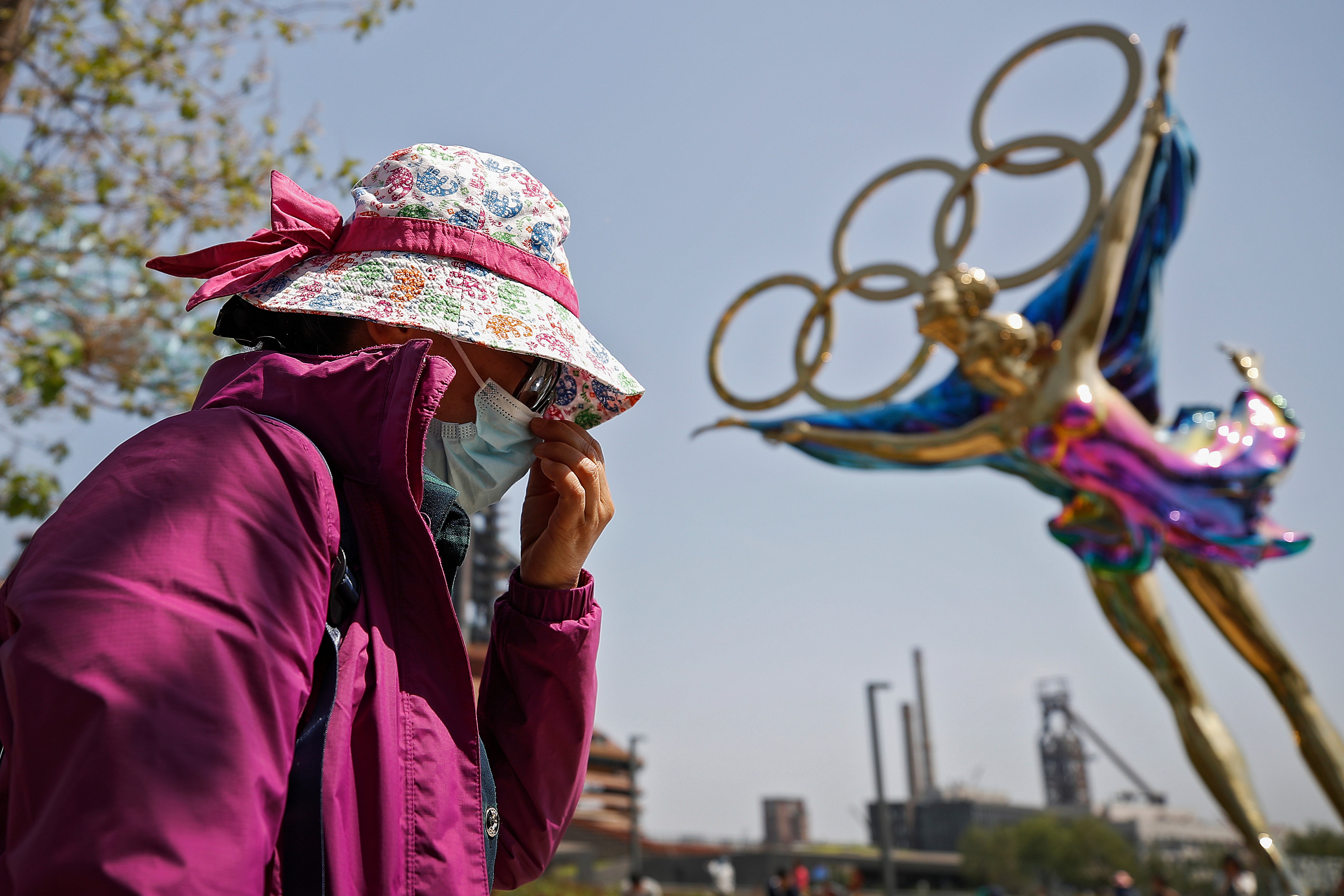 File: A woman adjusts her face mask as she walks by a statue featuring the Beijing Winter Olympics figure