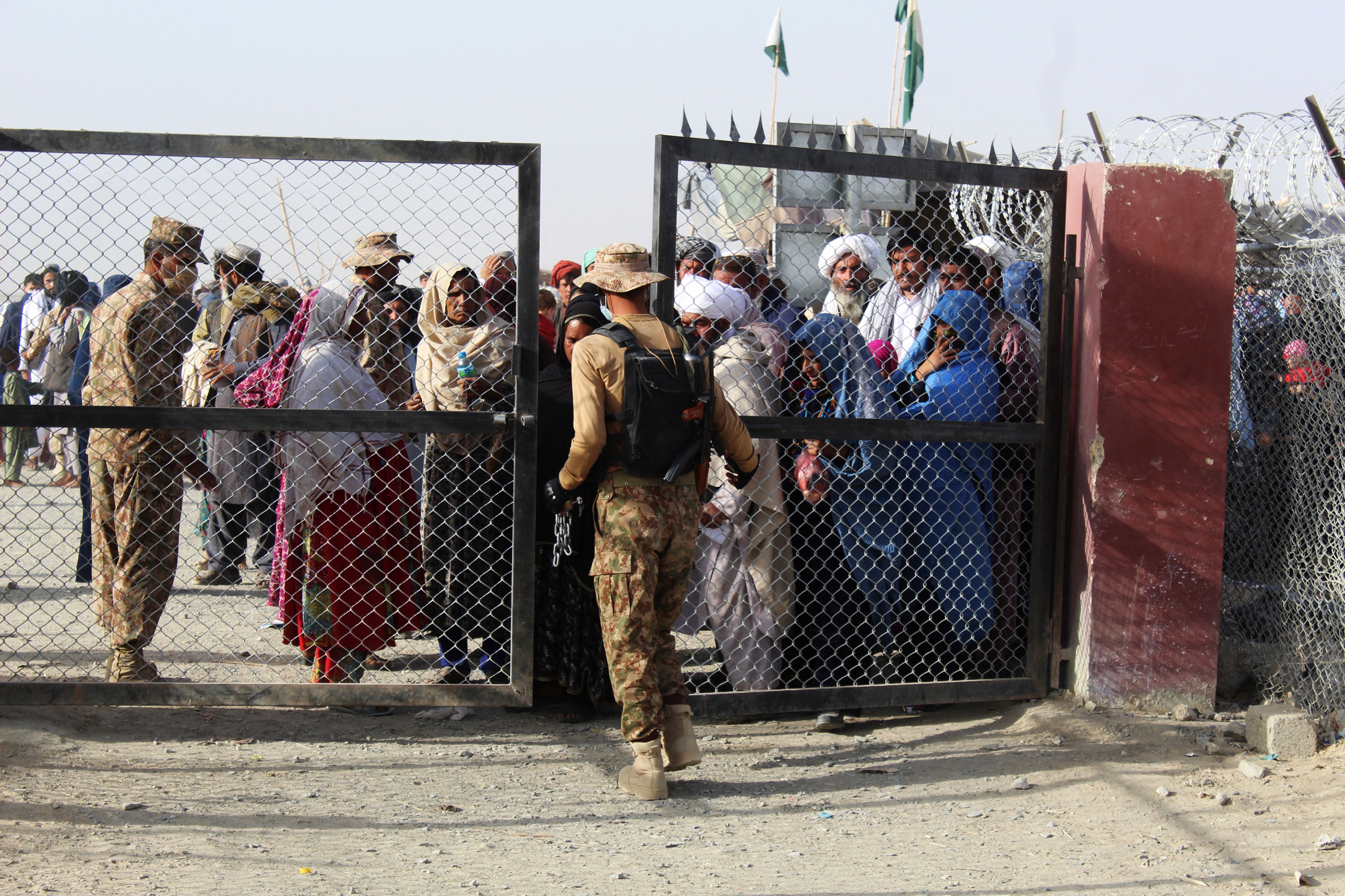 A Pakistani soldier holds a gate as Afghan and Pakistani people wait to enter Afghanistan through the Pakistan-Afghanistan border crossing point in Chaman