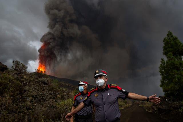 <p>A police officer ushers journalists back as the eruption on La Palma progresses down the hillside</p>