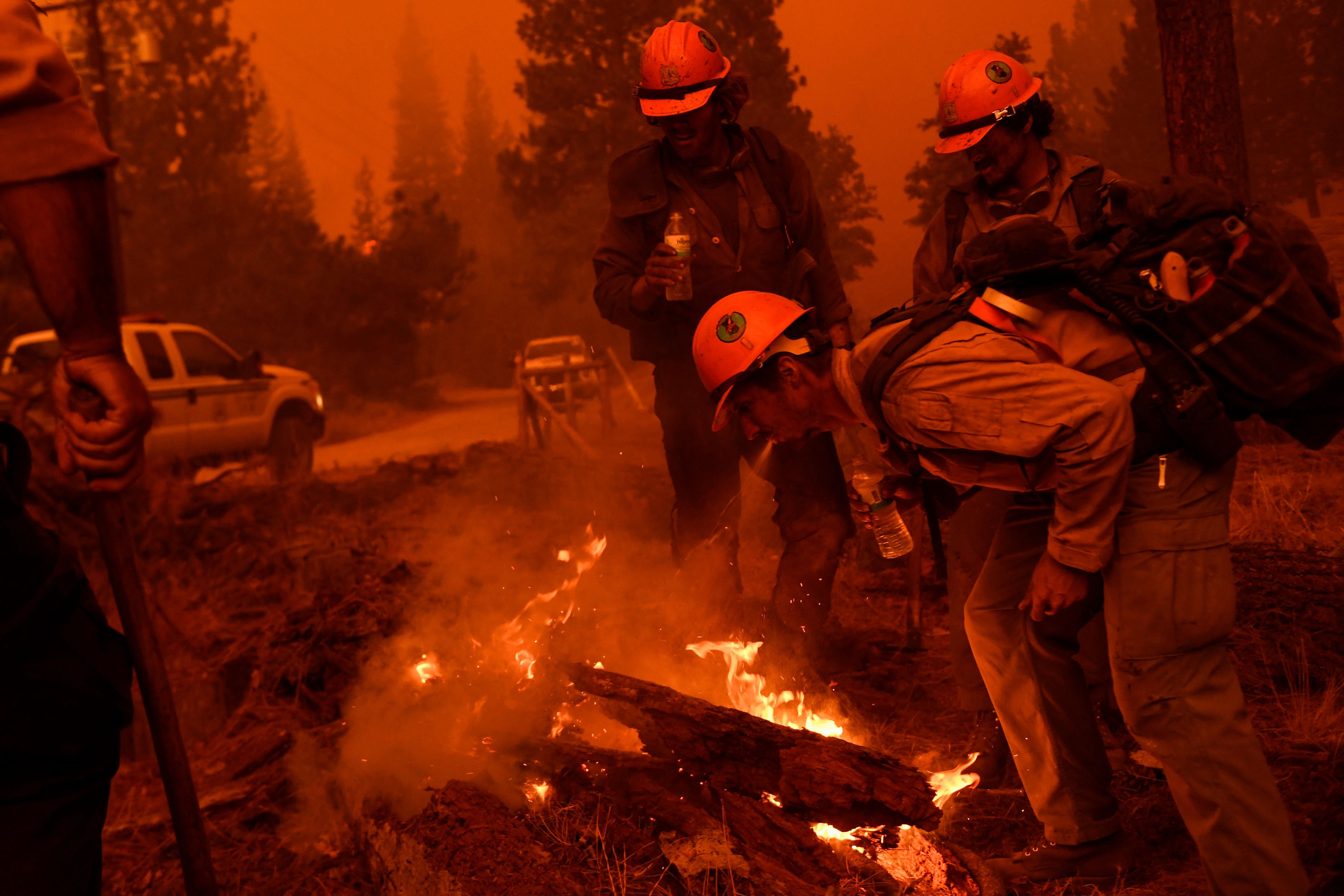Firefighters improvise and spray water from their mouths to control a small spot fire while waiting for a hose line during the Windy Fire in the Sequoia National Forest near Johnsondale, California on September 22, 2021