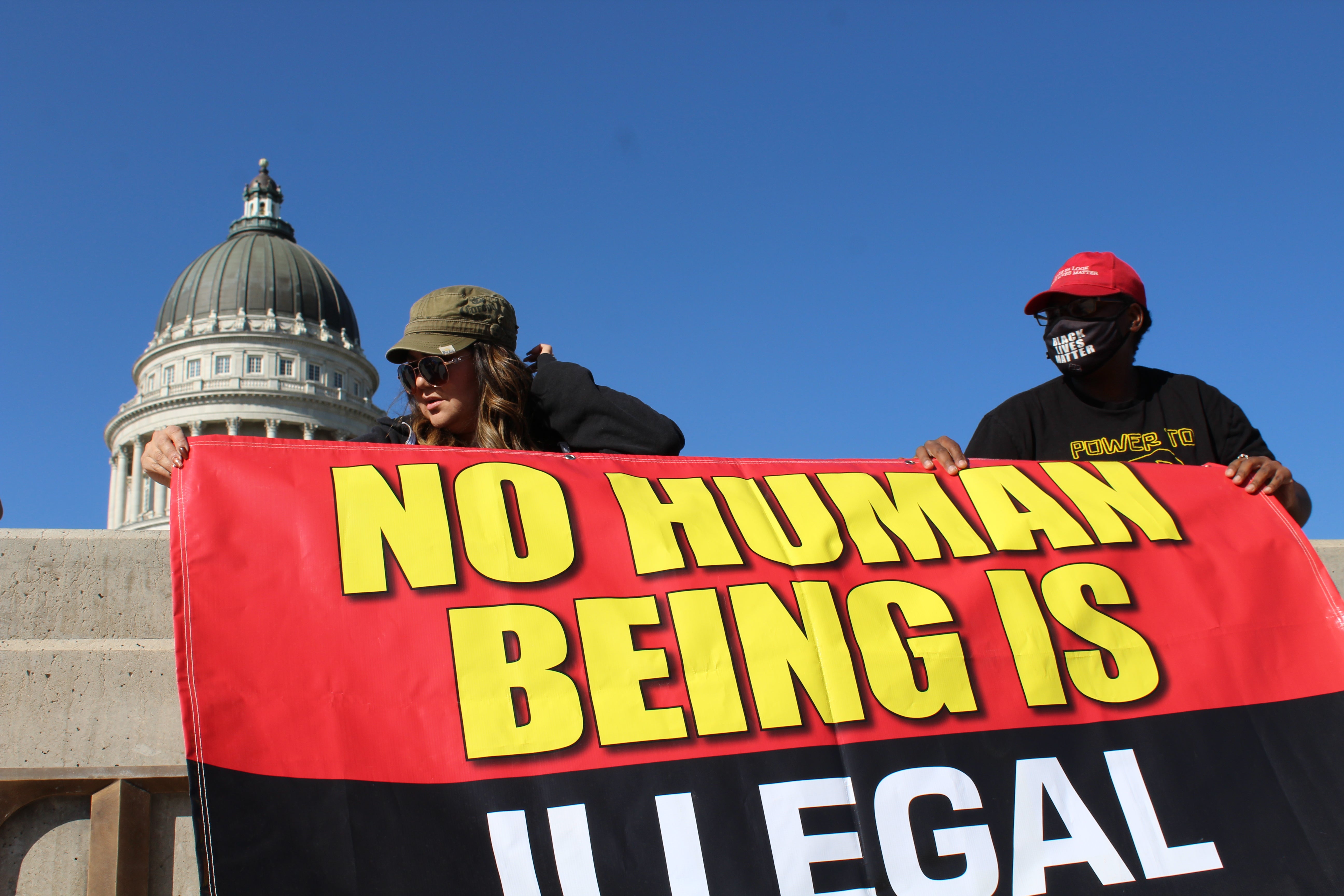 Activist Ma Black helps rally organizer Natasha Cadet put up a banner emblazoned with the message “No human being is illegal” at the Utah Capitol grounds.
