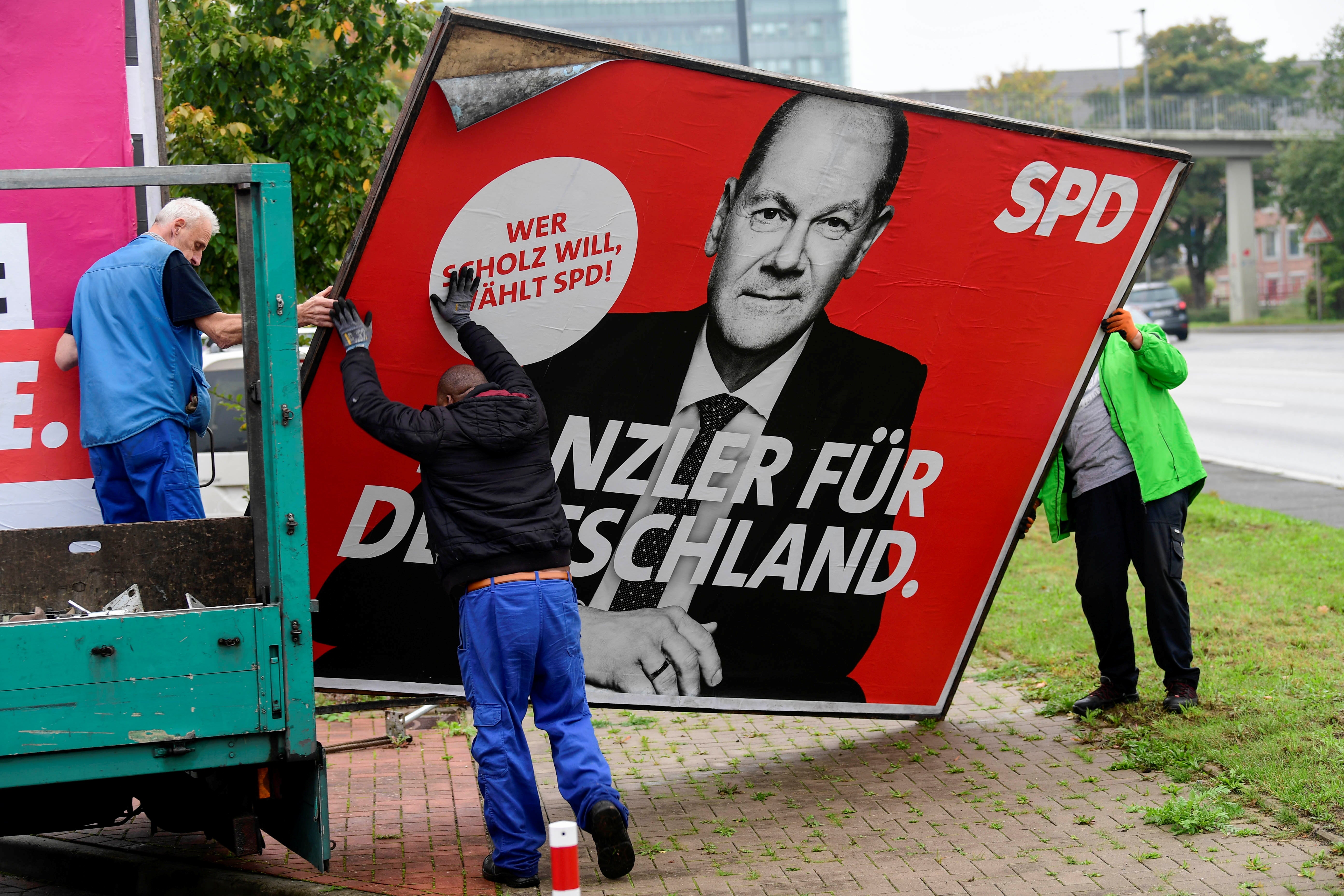 Workers remove a poster for the SPD’s Olaf Scholz, who is seeking a three-way coalition