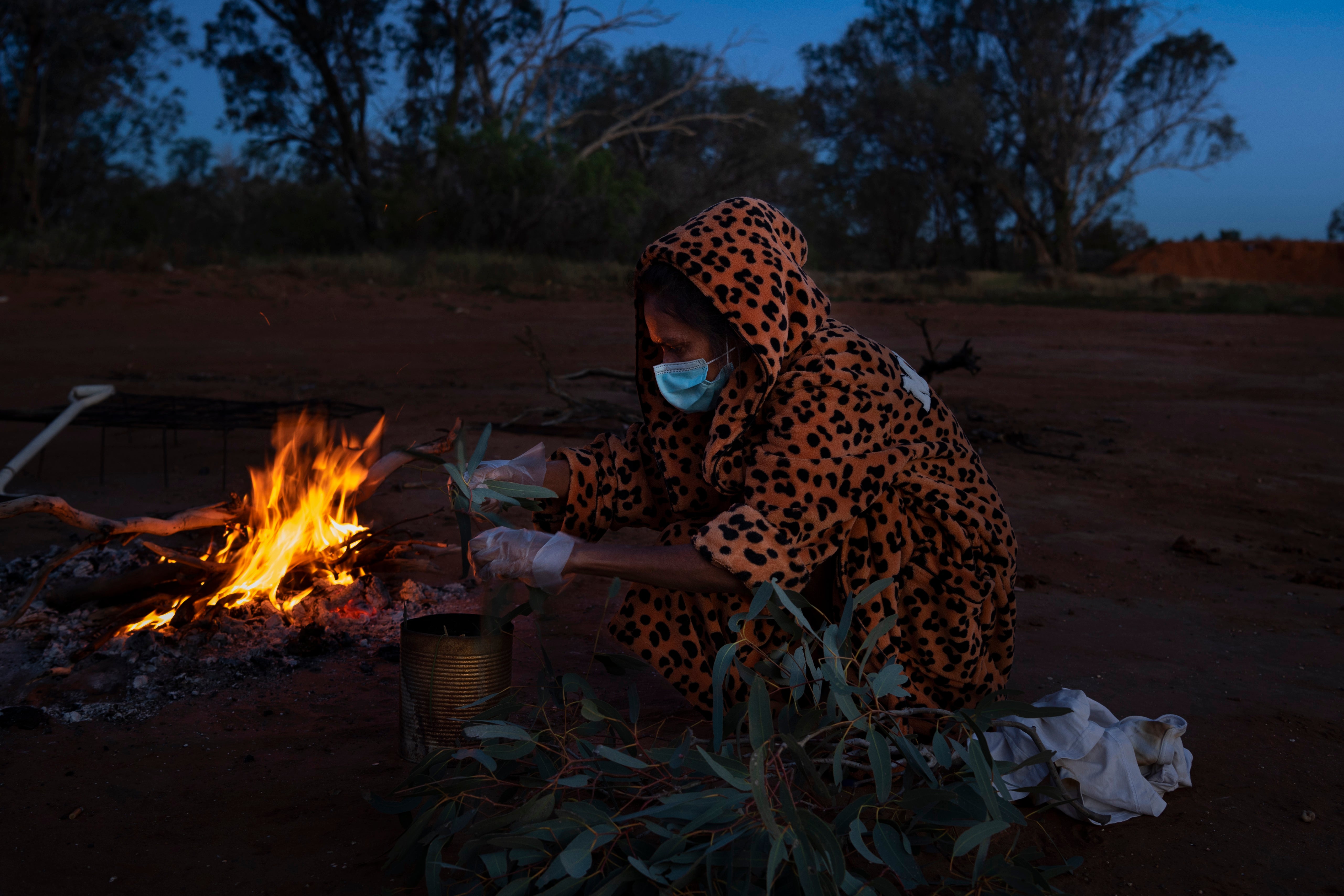 Patricia Wilson gathers eucalyptus leaves and other plants that she burned in a metal tin in an effort to ward off Covid-19 at the Warrawong campground in Wilcannia