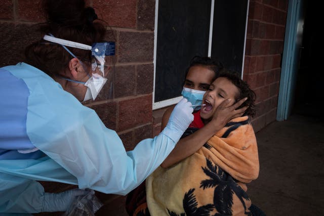 <p>Brooke Johnson holds her son Christopher while a New South Wales Health worker takes a Covid swab</p>