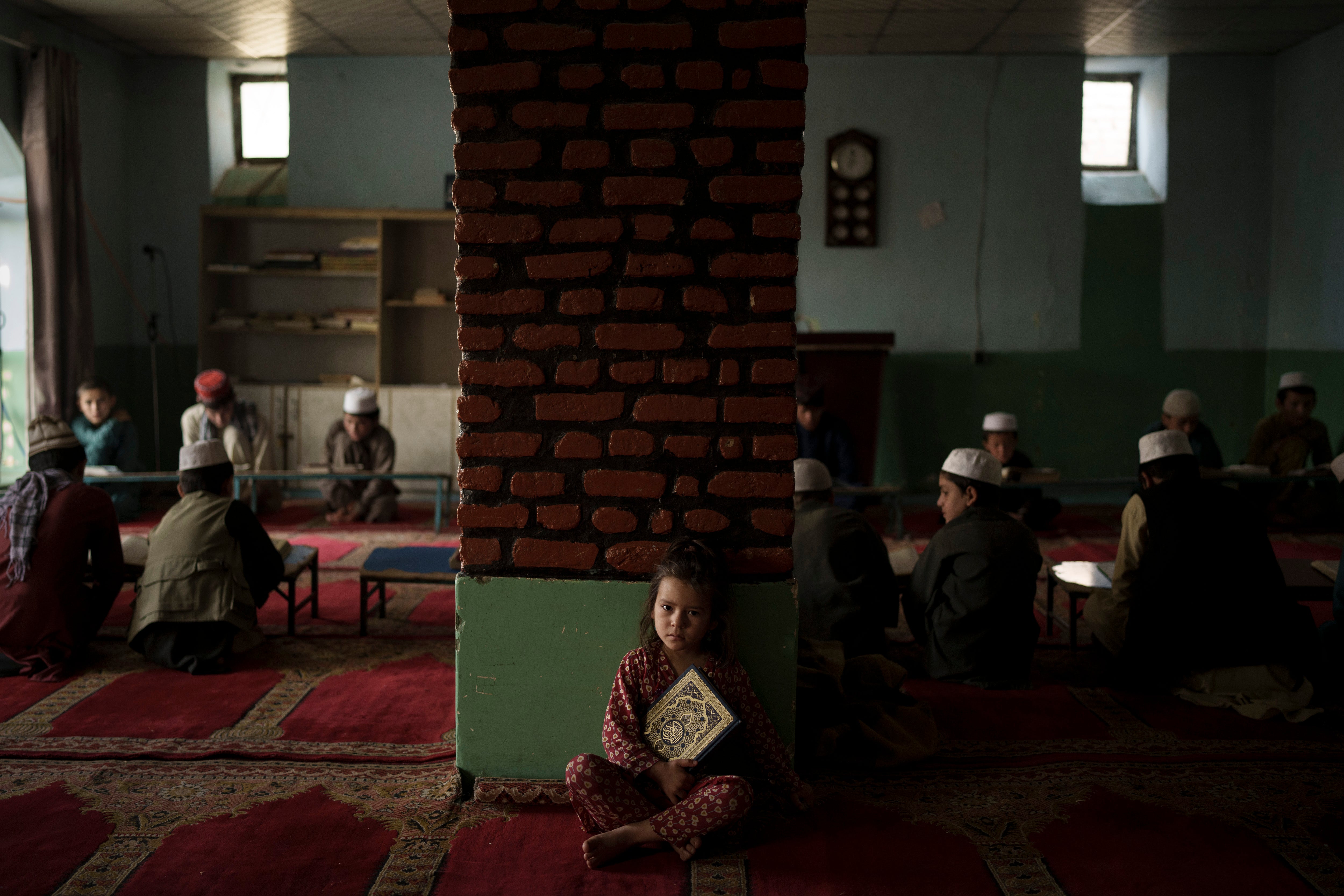 The niece of a teacher sits alone in a classroom as boys attend a class to memorise the Quran, Islam's holy book, at a madrasa in Kabul