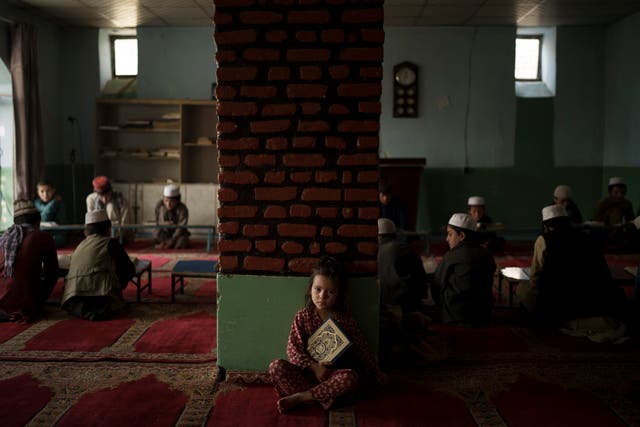 <p>The niece of a teacher sits alone in a classroom as boys attend a class to memorise the Quran, Islam's holy book, at a madrasa in Kabul</p>