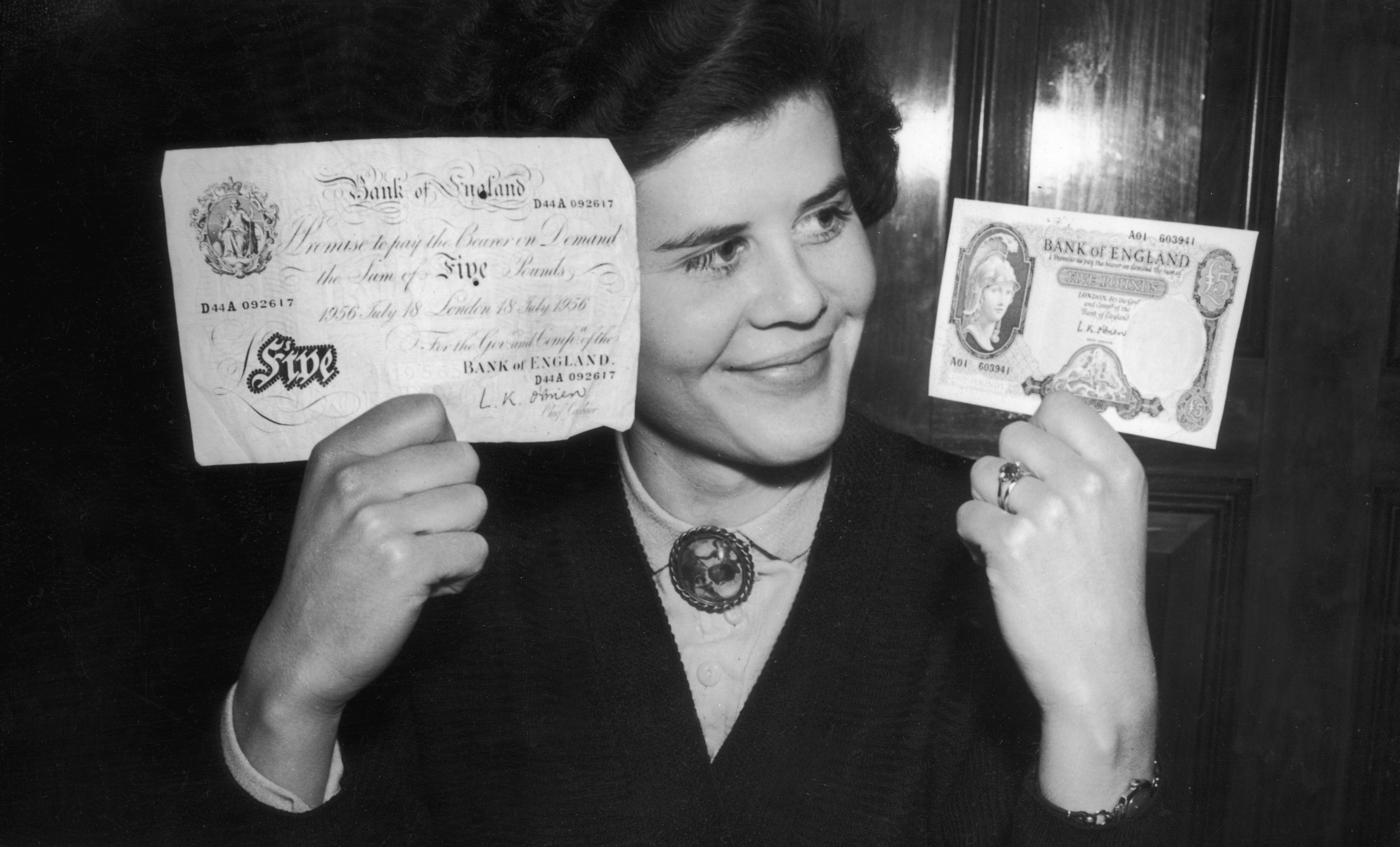 21 February 1957: Deirdre Denbigh compares Britain’s old five pound note (left) with its smaller replacement on the day of its introduction