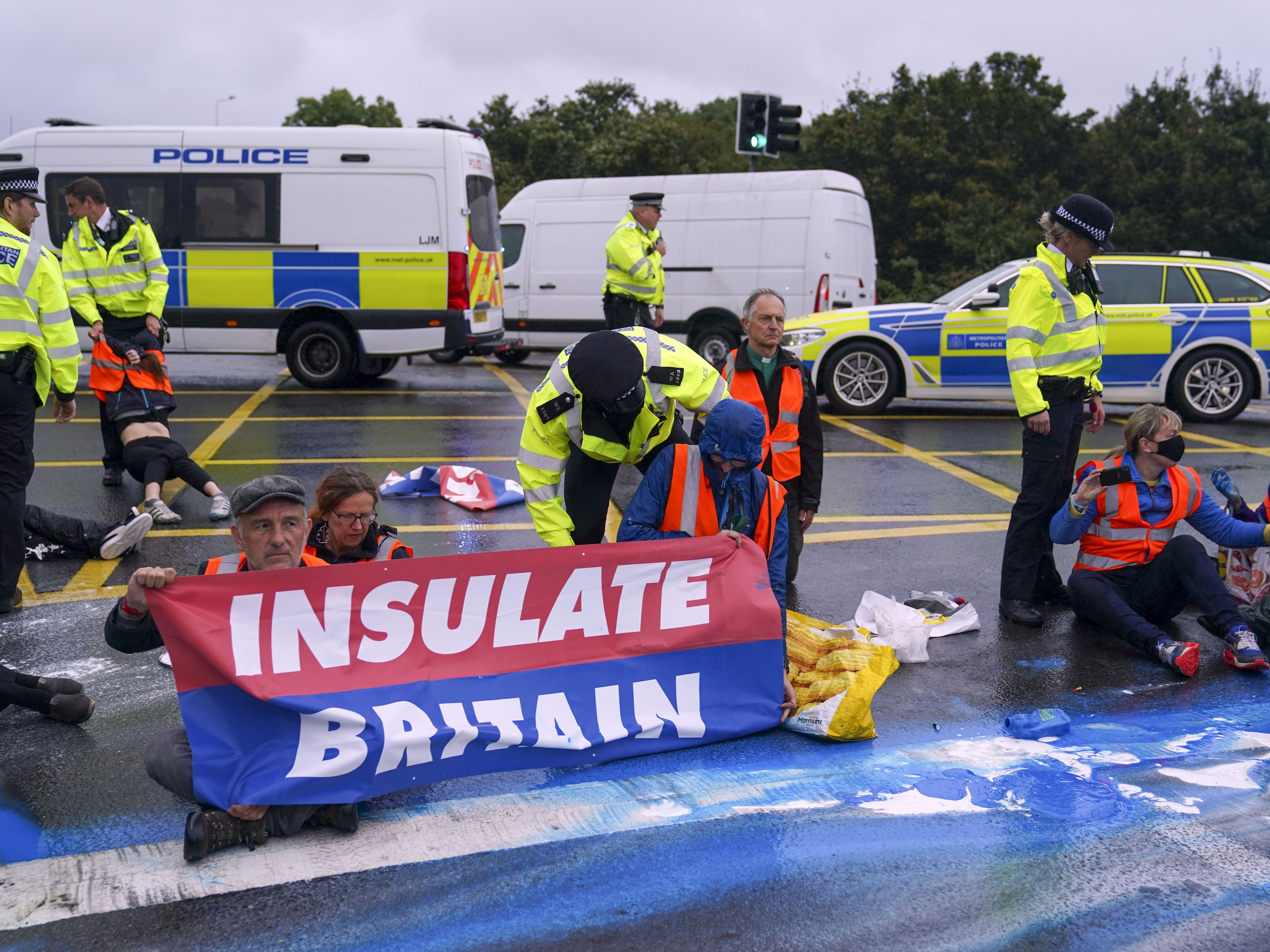 Police officers detain a protester from Insulate Britain occupying a roundabout leading from the M25 motorway