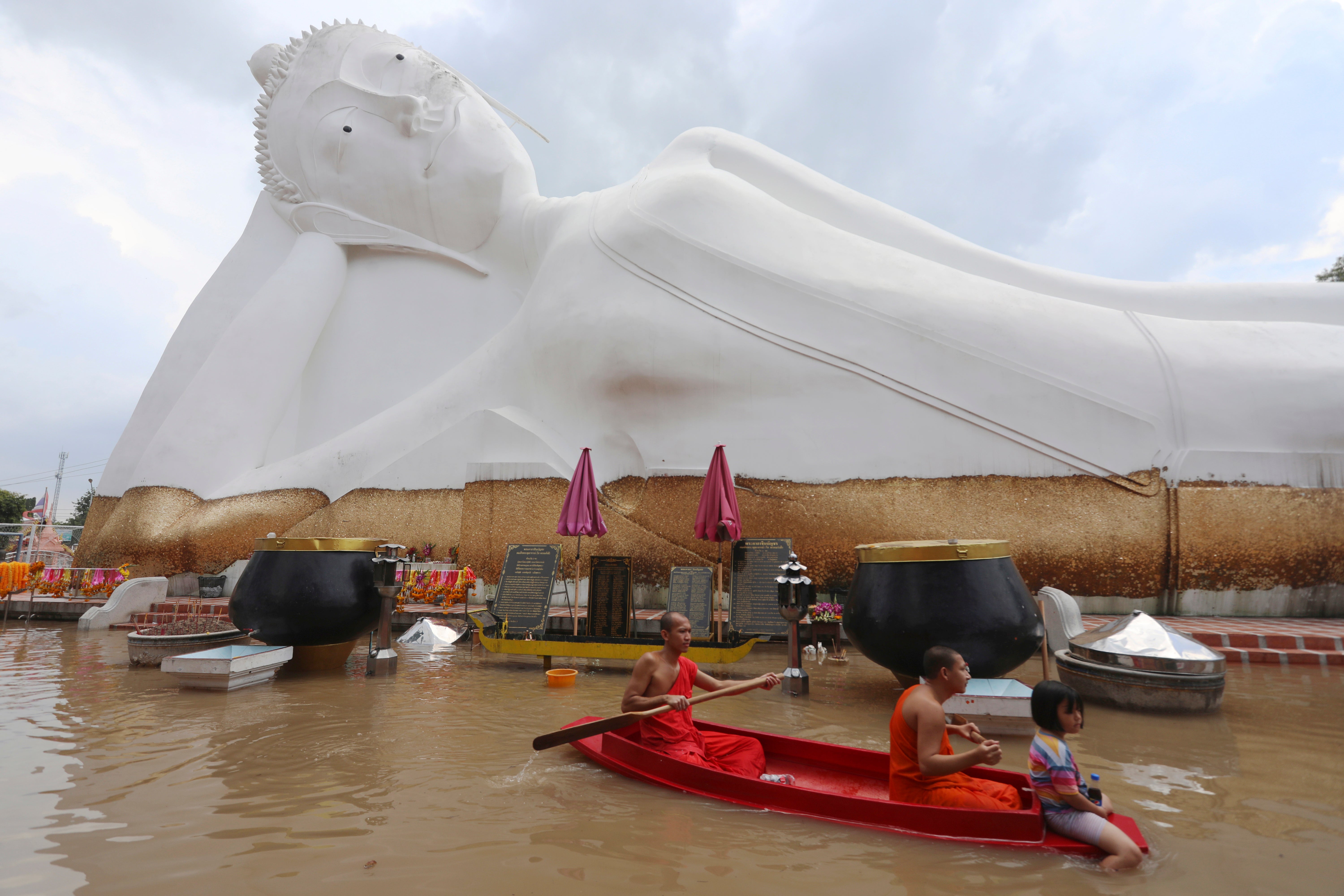 Buddhist monks paddle a boat through floodwaters in front of a reclining Buddha at the Wat Satue in Ayutthaya province.