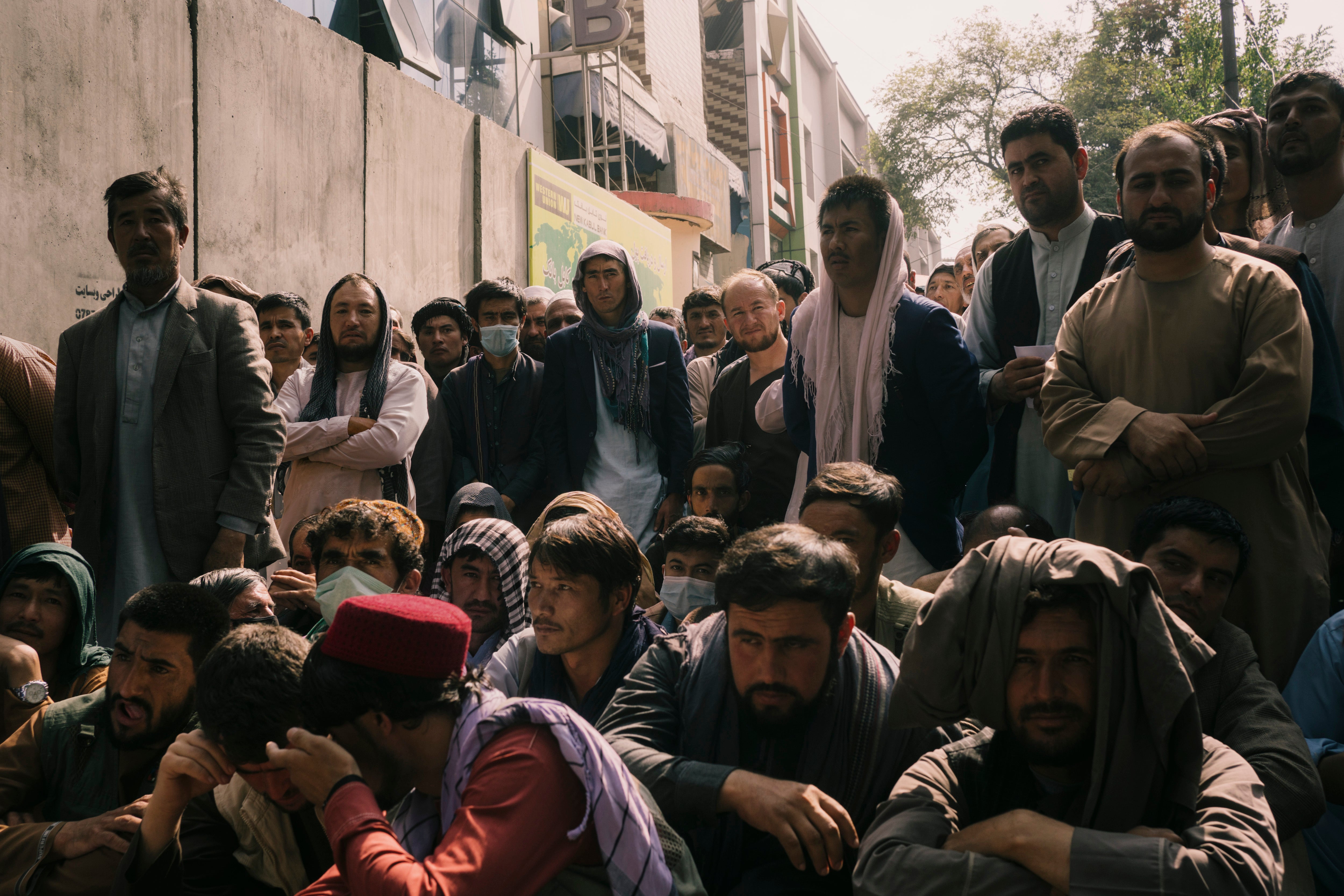 Holders of bank accounts wait in front of a Kabul bank