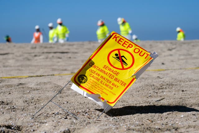 <p>A warning sign is displayed as workers in protective suits clean the contaminated beach after an oil spill in Huntington Beach, Calif., on Tuesday, Oct. 5, 2021. </p>