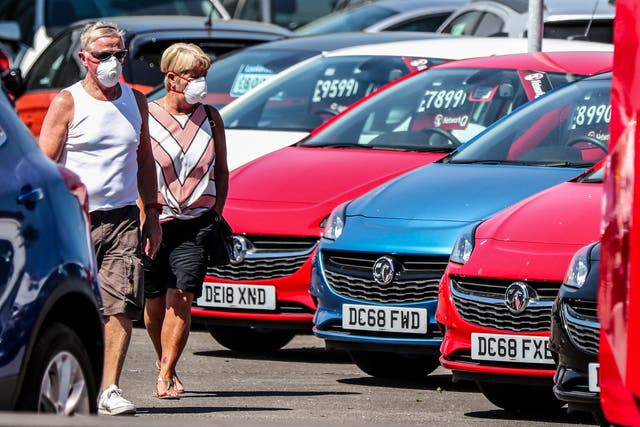 A couple walk past cars on the forecourt of Vauxhall Lookers in Speke, Liverpool (Peter Byrne/PA)