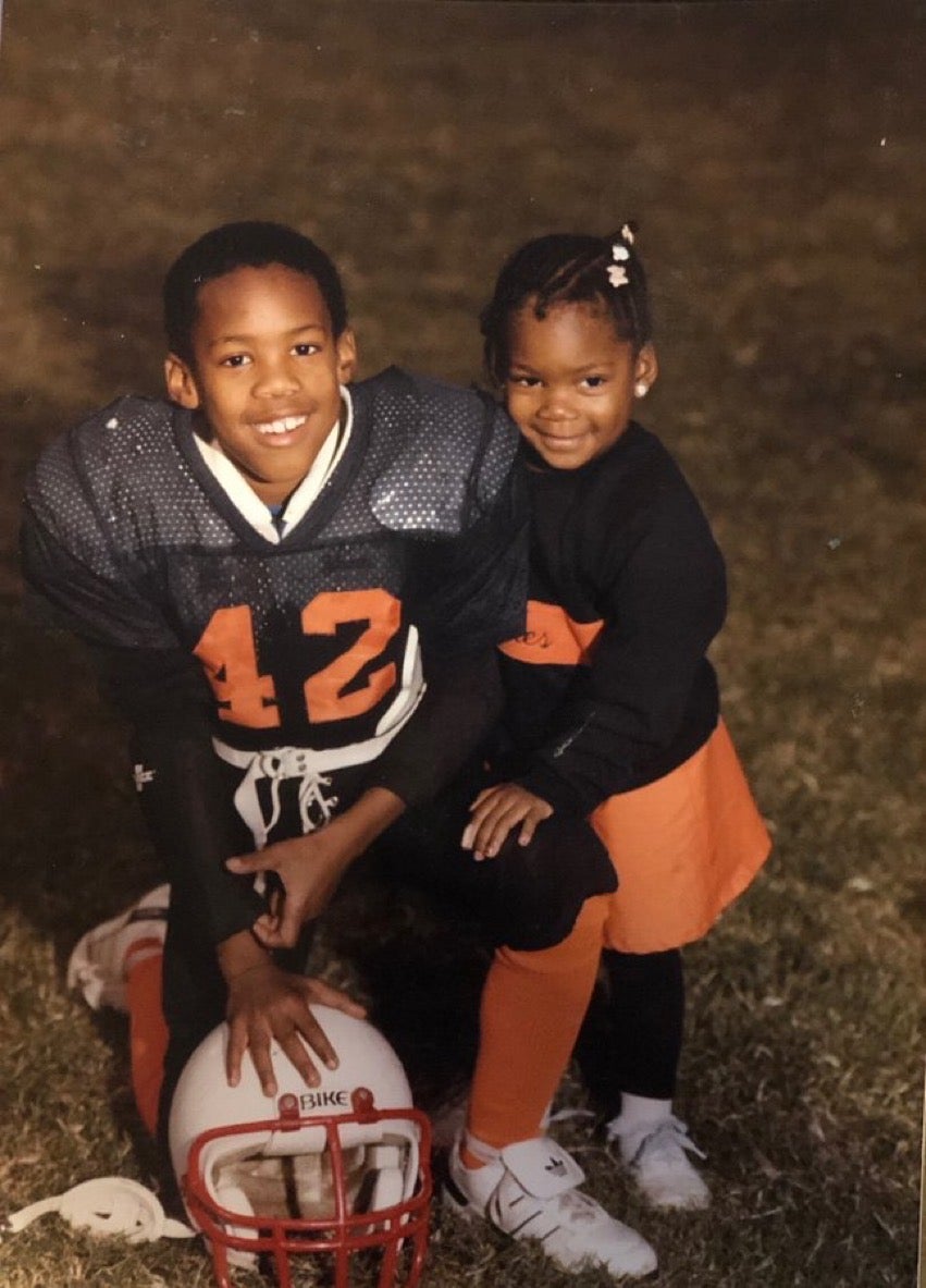 Julius Jones as a child, posing with his sister while wearing his football uniform.