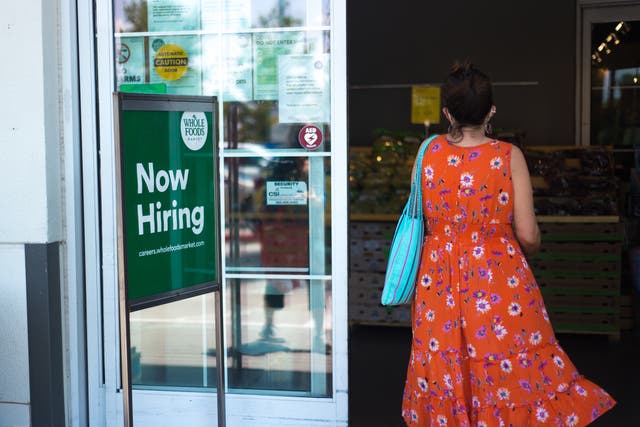 <p>A woman walks into a Whole Foods supermarket in Santa Fe, New Mexico, past a ‘Now Hiring’ sign</p>