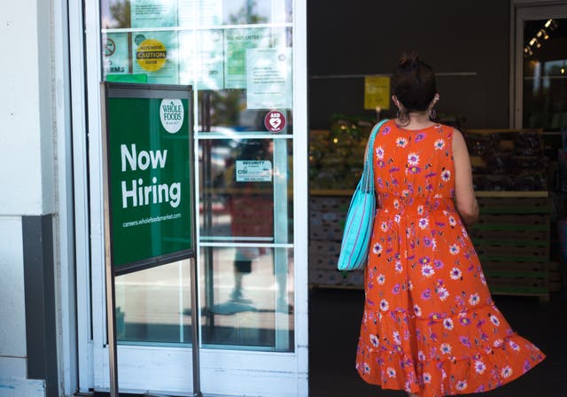 <p>A woman walks into a Whole Foods supermarket in Santa Fe, New Mexico, past a ‘Now Hiring’ sign</p>