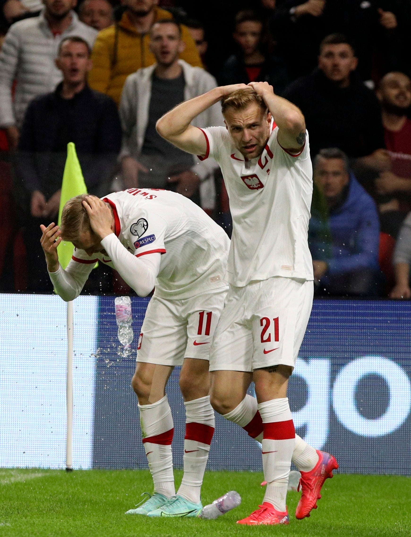 Poland’s Karol Swiderski, left, holds his head as fans throw missiles on to the pitch following his goal (Franc Zhurda/AP)