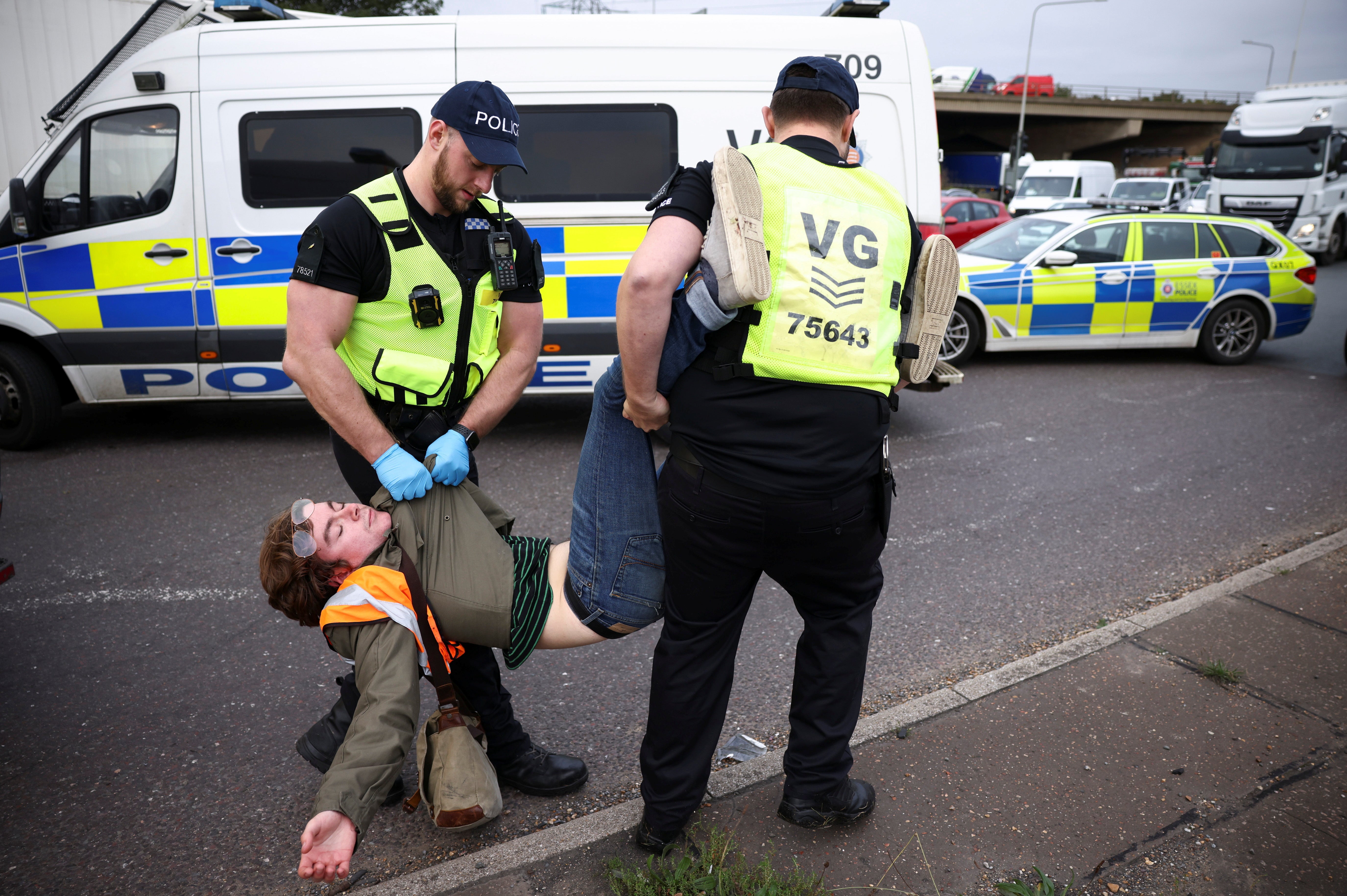 Police officers detain a man as Insulate Britain activists block a roundabout at a junction on the M25