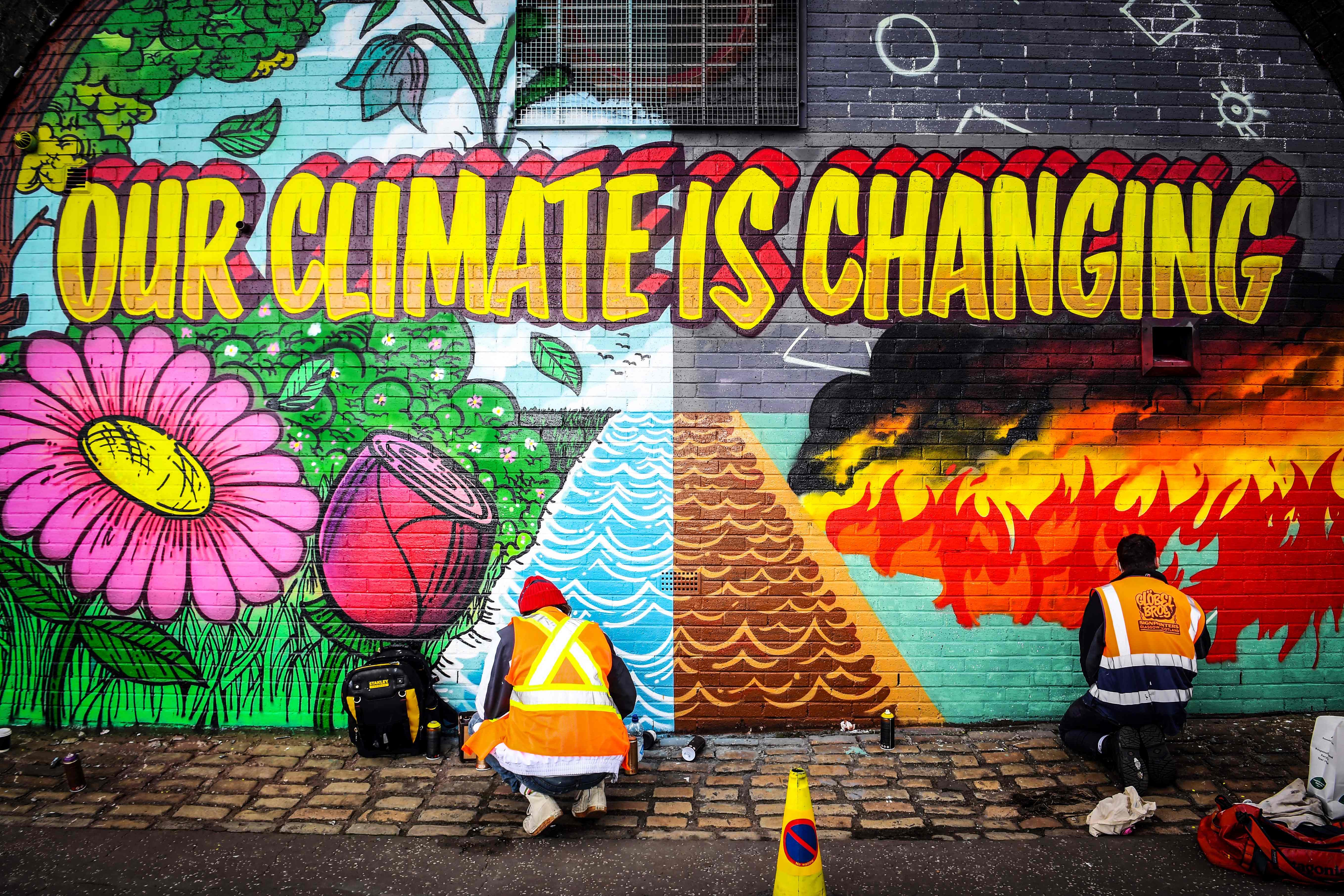 Street artists paint a mural on a wall opposite the Cop26 climate summit venue in Glasgow