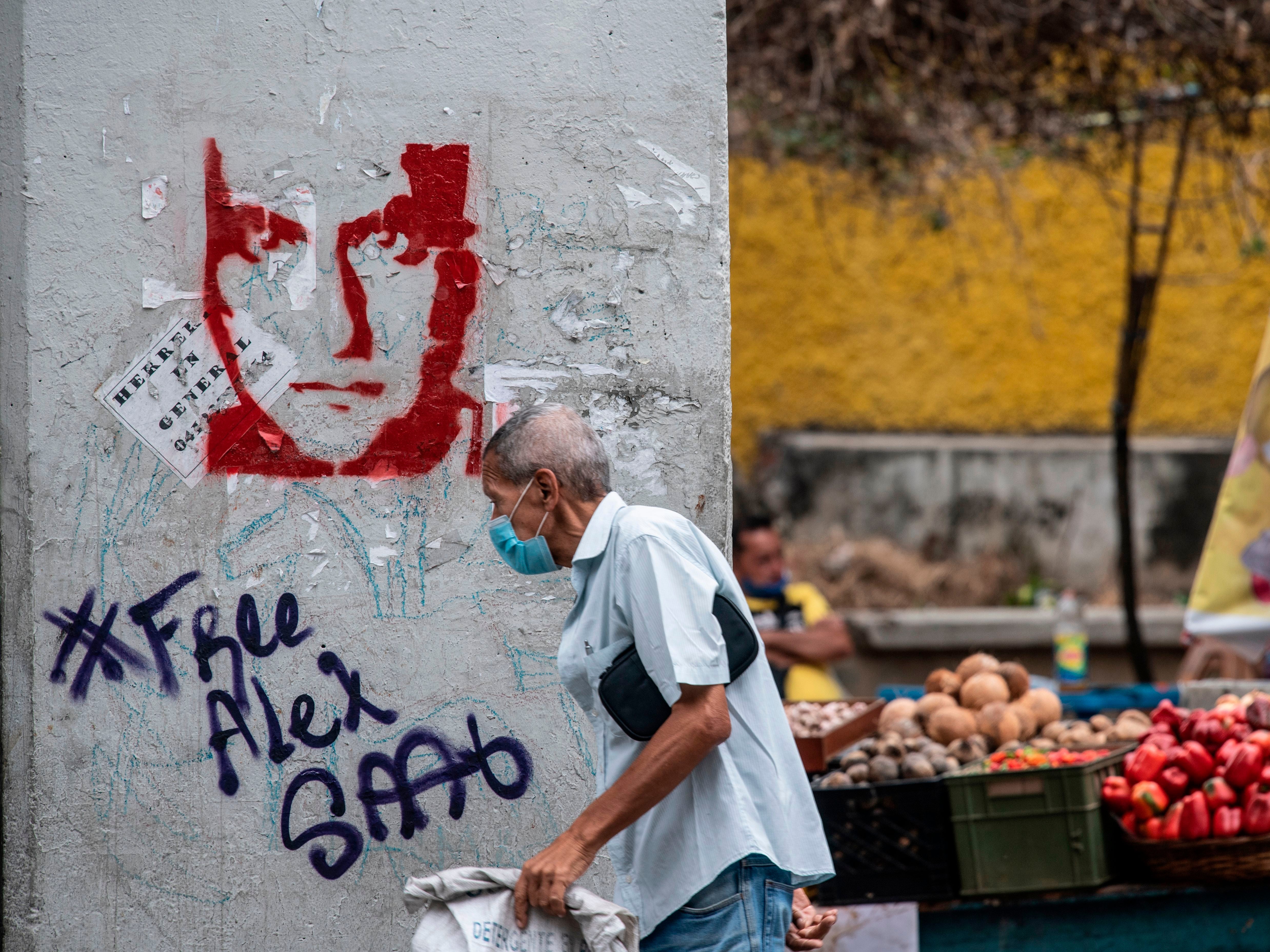 A man walks past graffiti in Caracas demanding Colombian businessman Alex Saab’s freedom