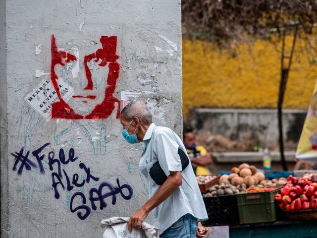 <p>A man walks past graffiti in Caracas demanding Colombian businessman Alex Saab’s freedom</p>