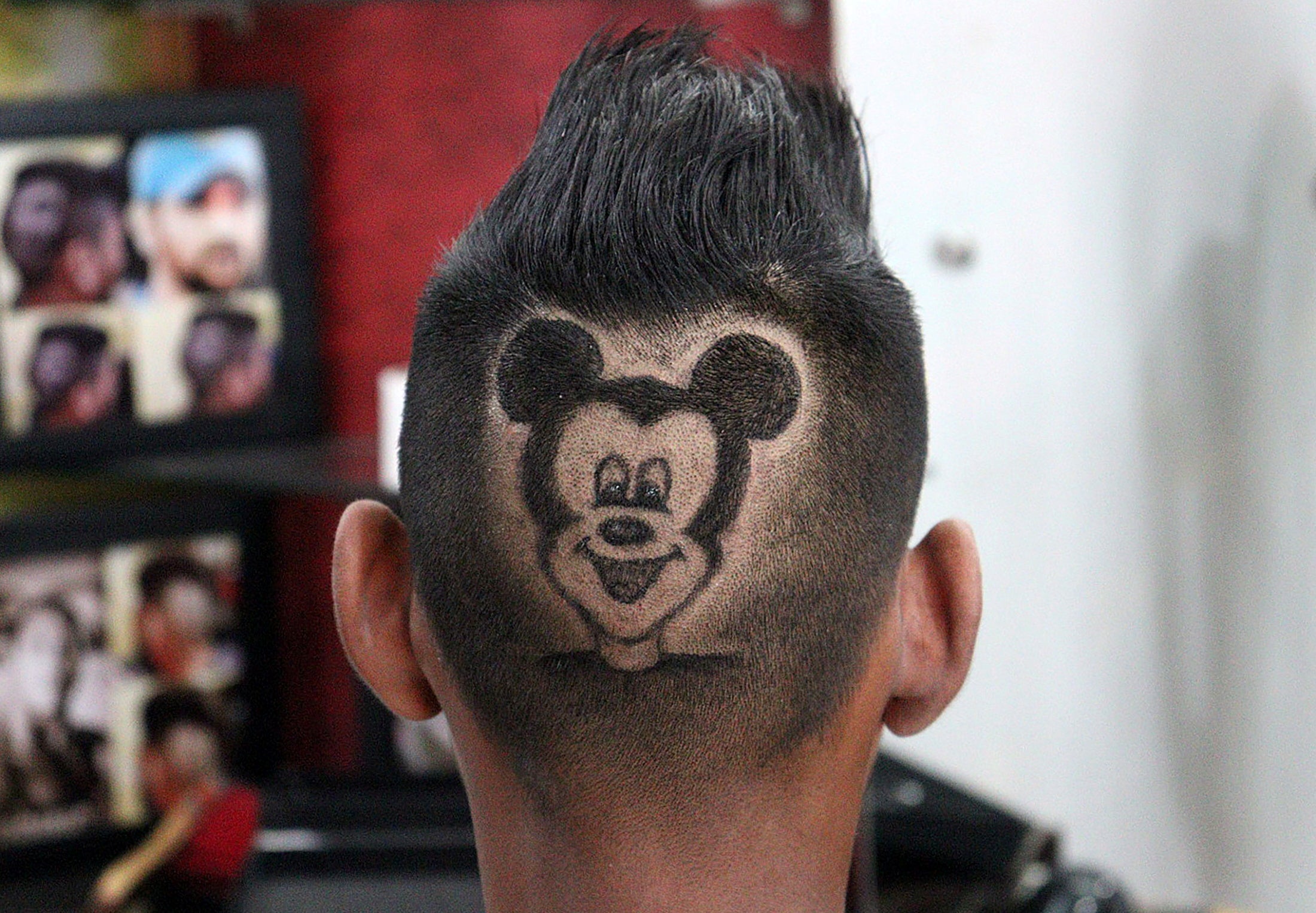 A customer poses for a photograph after he has his head shaved in the shape of Mickey Mouse by barber Rajwinder Singh Sidhu in India