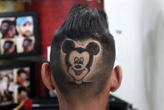 <p>A customer poses for a photograph after he has his head shaved in the shape of Mickey Mouse by barber Rajwinder Singh Sidhu in India</p>