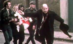 Father Edward Daly waves a blood-stained white handkerchief as he escorts a mortally-wounded protester to safety on Bloody Sunday