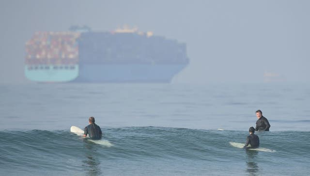 <p>Surfers wait for waves at Huntington Beach, California, as a container ship queues offshore</p>