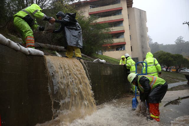 <p>Workers try to divert water into drains as rain pours down in Marin City, California</p>