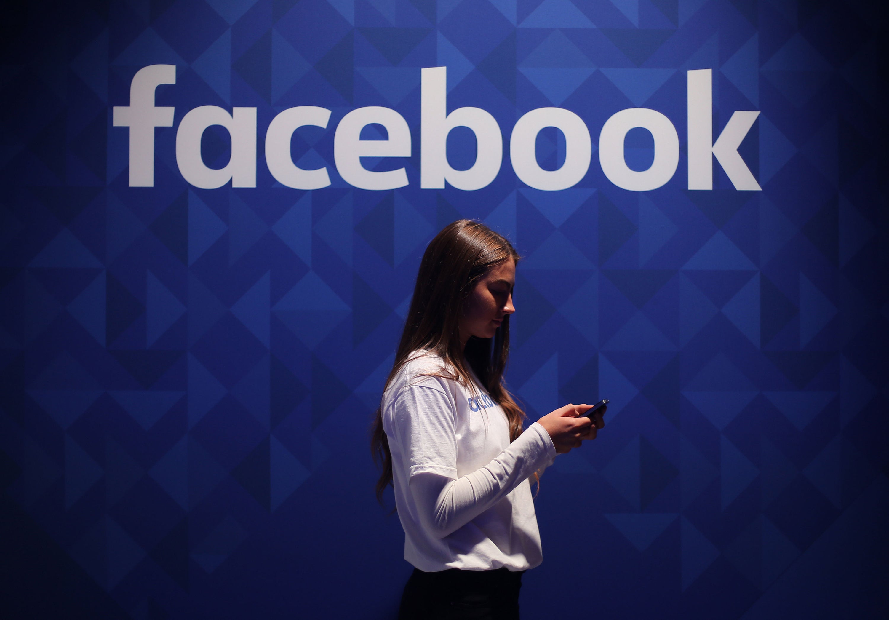 Una mujer que usa su teléfono bajo un logo de Facebook (Niall Carson / PA)