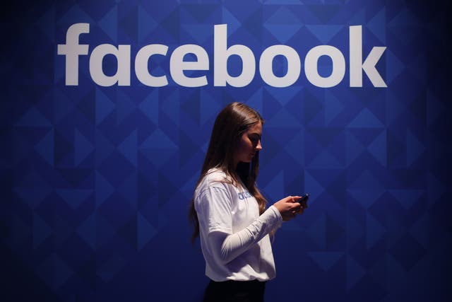 A woman using her phone under a logo of Facebook (Niall Carson/PA)