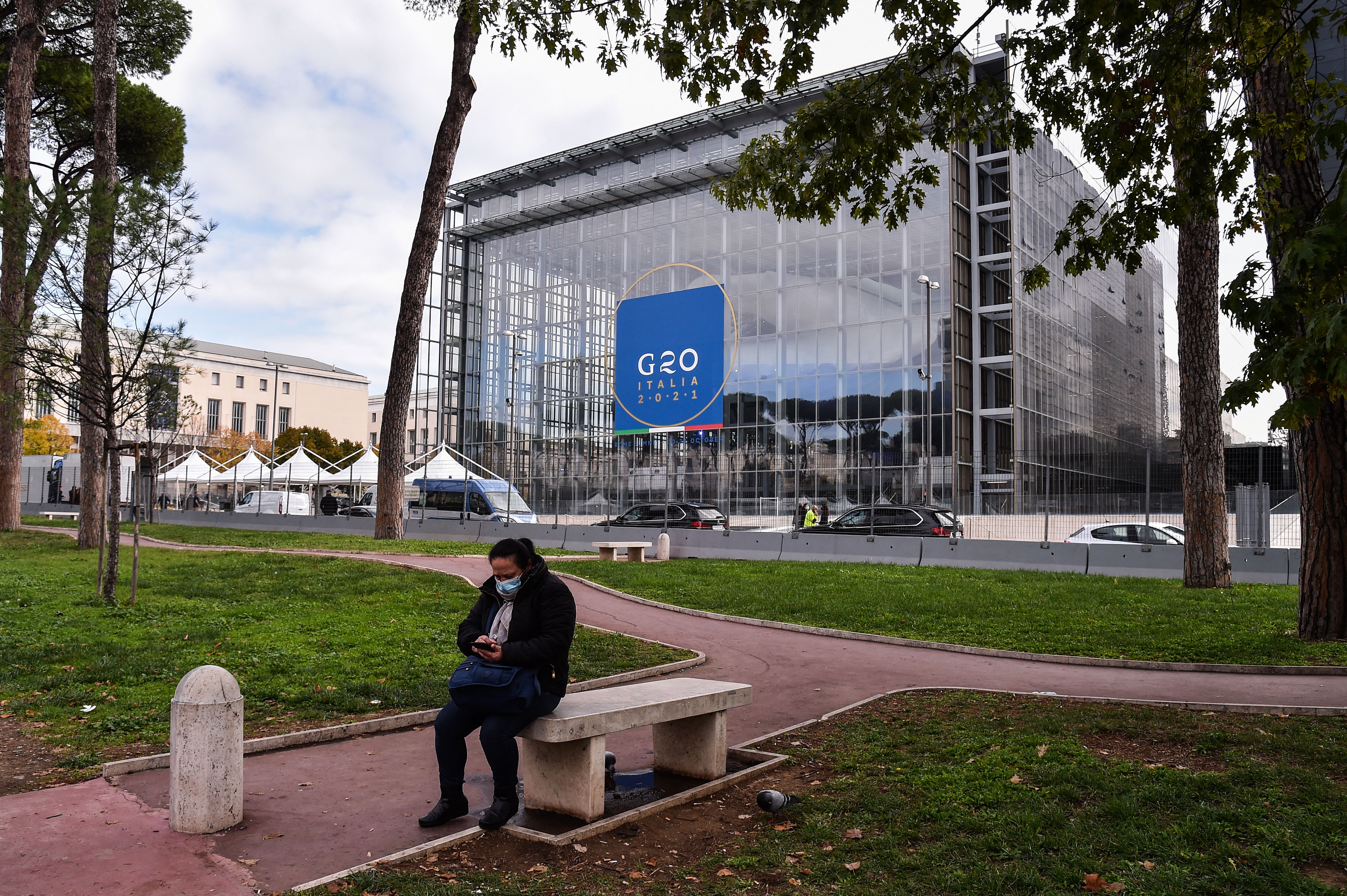 A woman checks her phone in a park opposite the convention centre ‘La Nuvola’