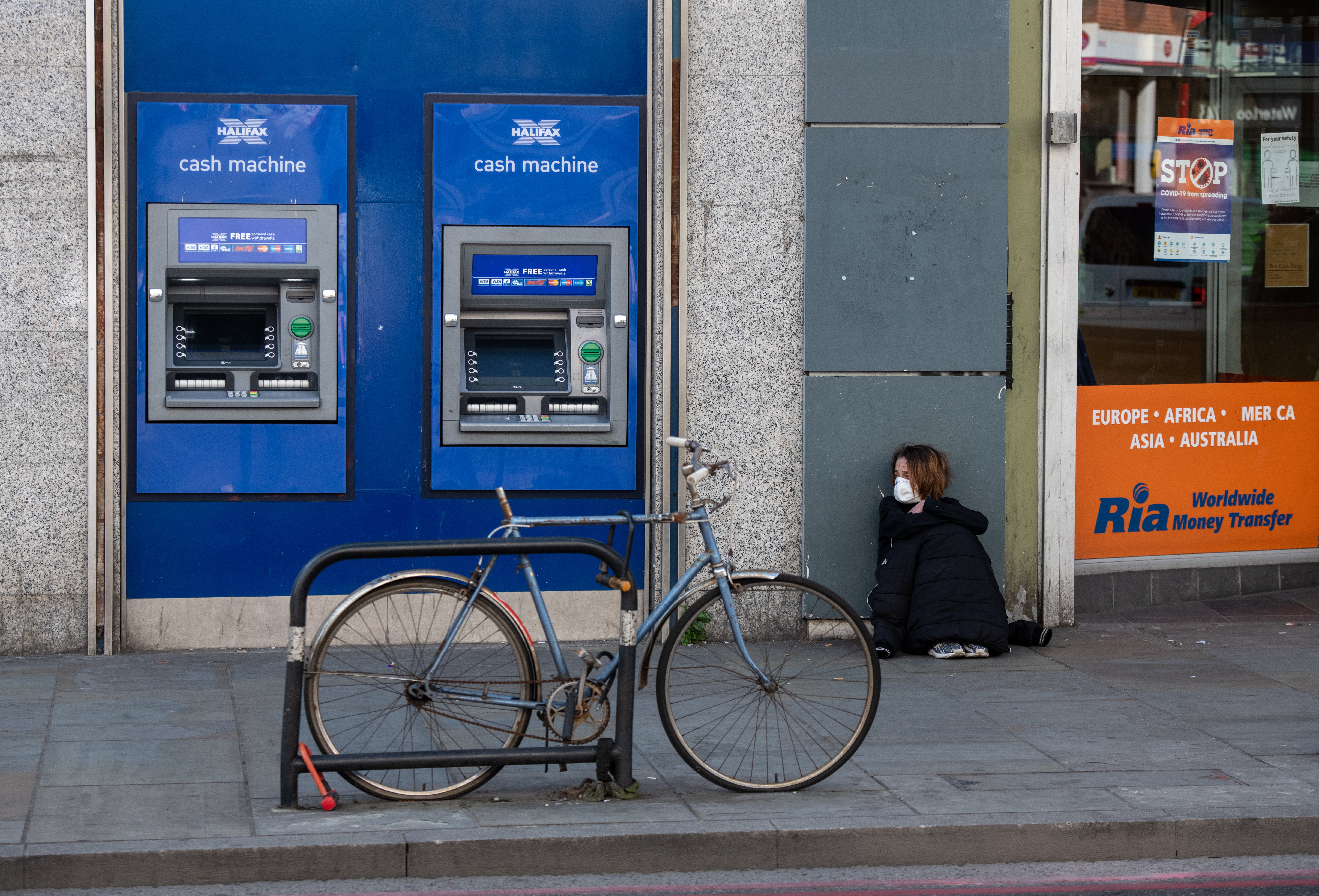 A homeless woman sits next to cash machines in Dalston in east London in April 2020
