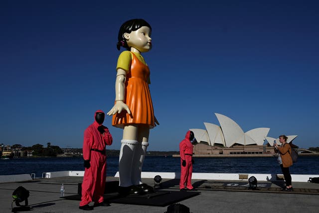 <p>Cosplayers stand next to a 4.5 metre tall replica doll from the Netflix series “Squid Game” on display at the harbour in Sydney </p>